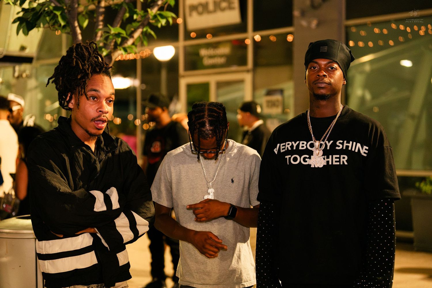 Three young men posing together outside at night near a police station.