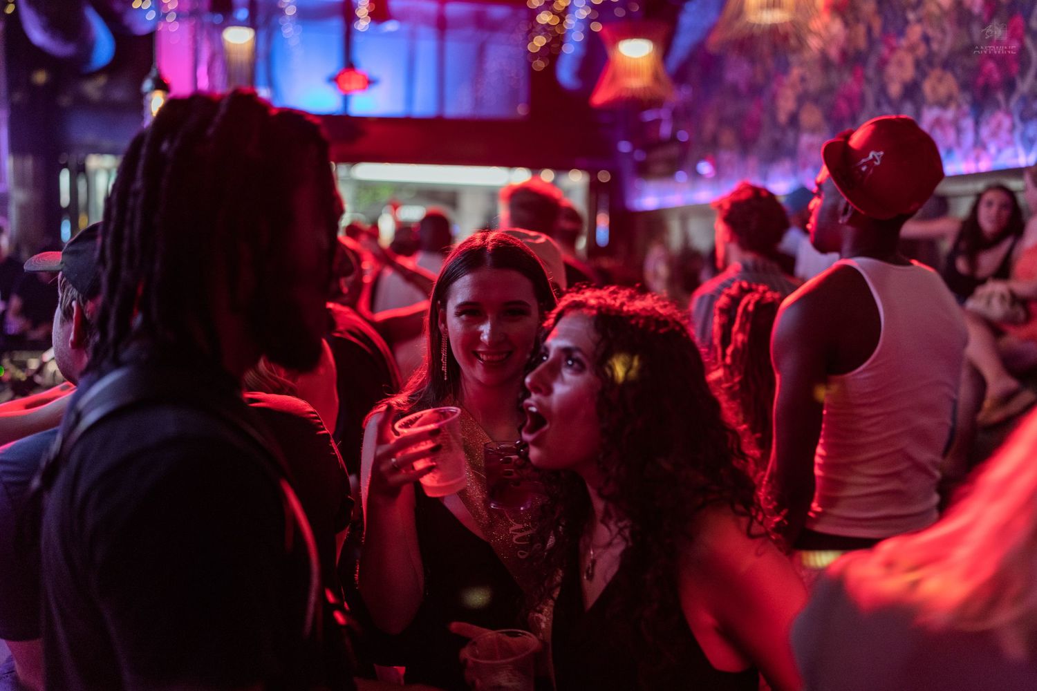 Group of friends socializing in crowded red-lit nightclub dance floor setting.