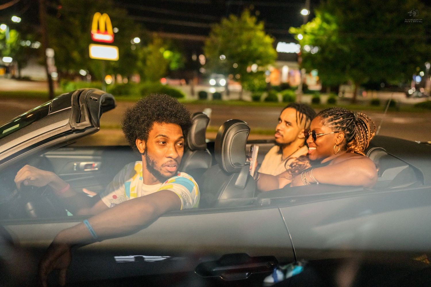 Group of friends sitting in a convertible car at night outside a McDonald's restaurant.
