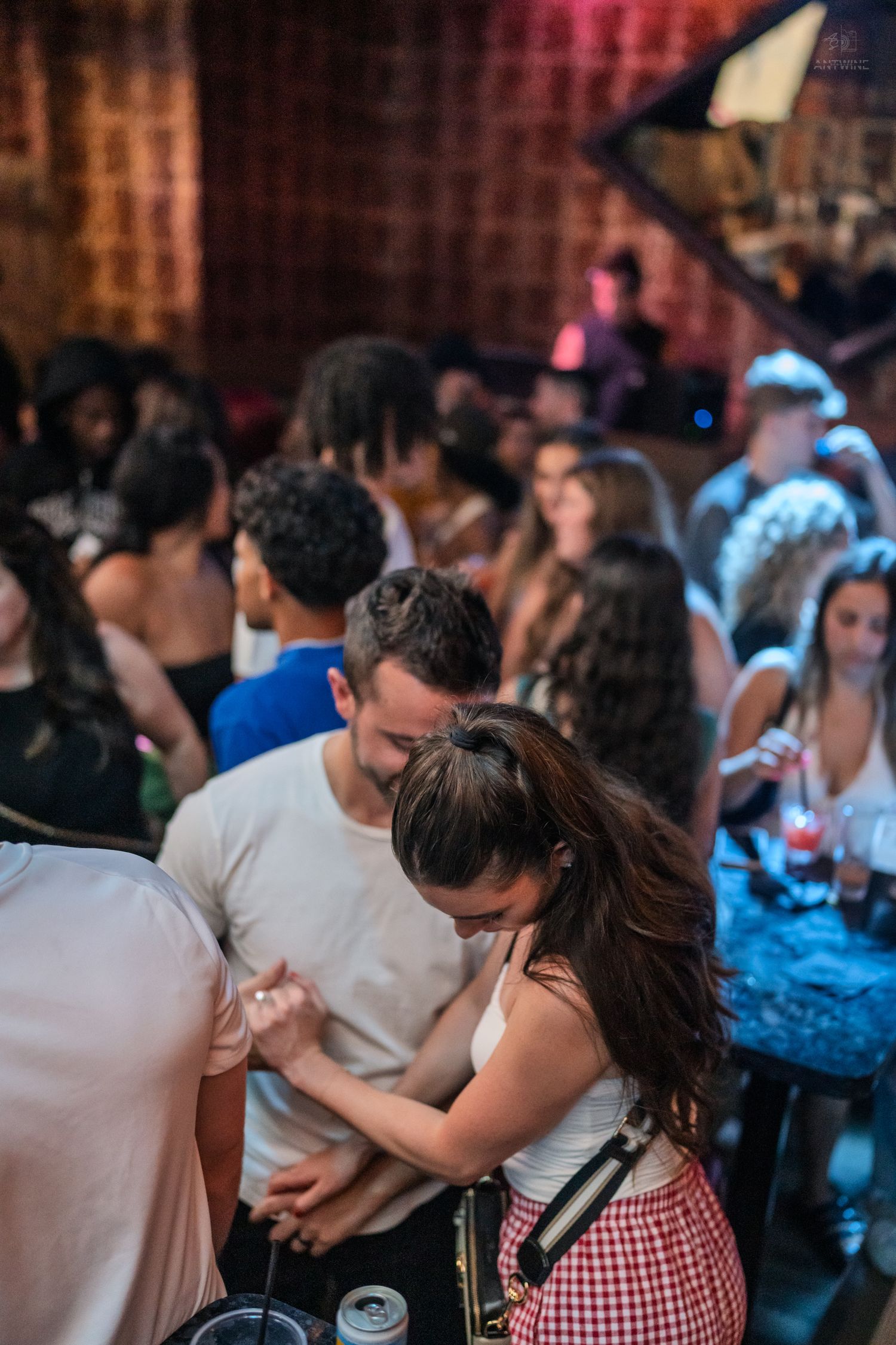 Couple dancing closely together in a busy nightclub with warm ambient lighting and crowd in background.