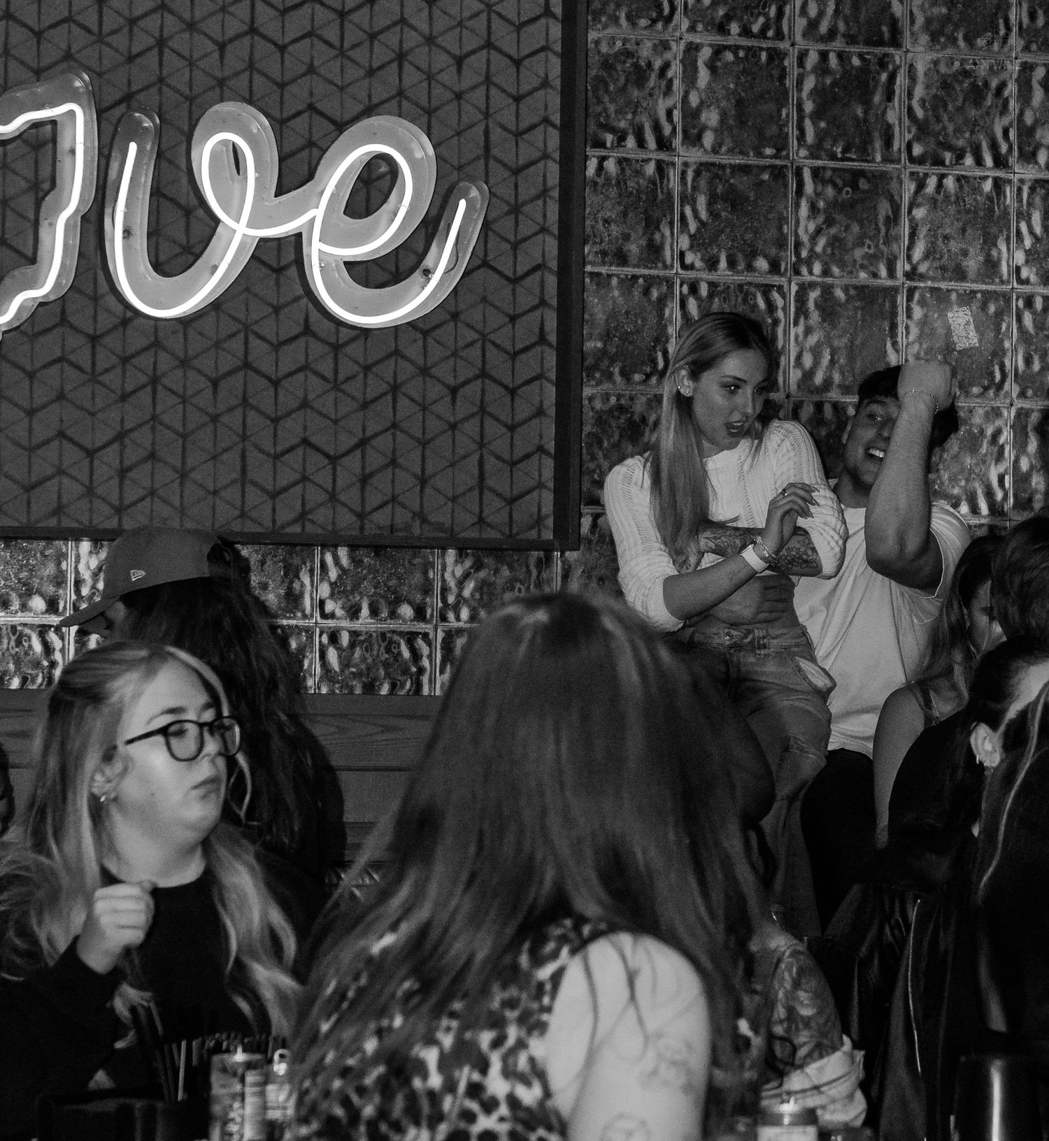 Black and white photo of women socializing at a bar with a neon love sign.