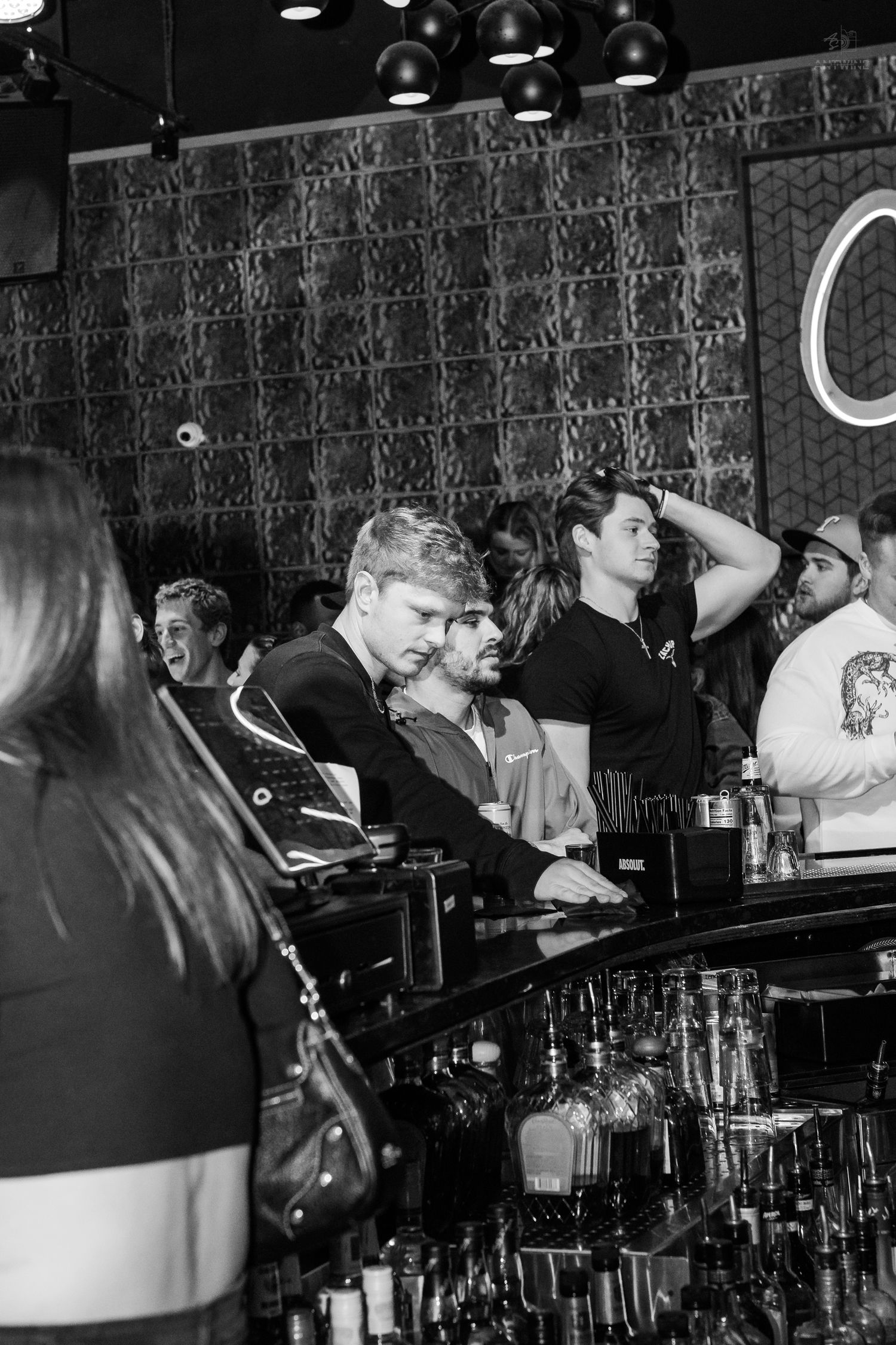 Black and white photo of patrons waiting at a busy nightclub bar counter.