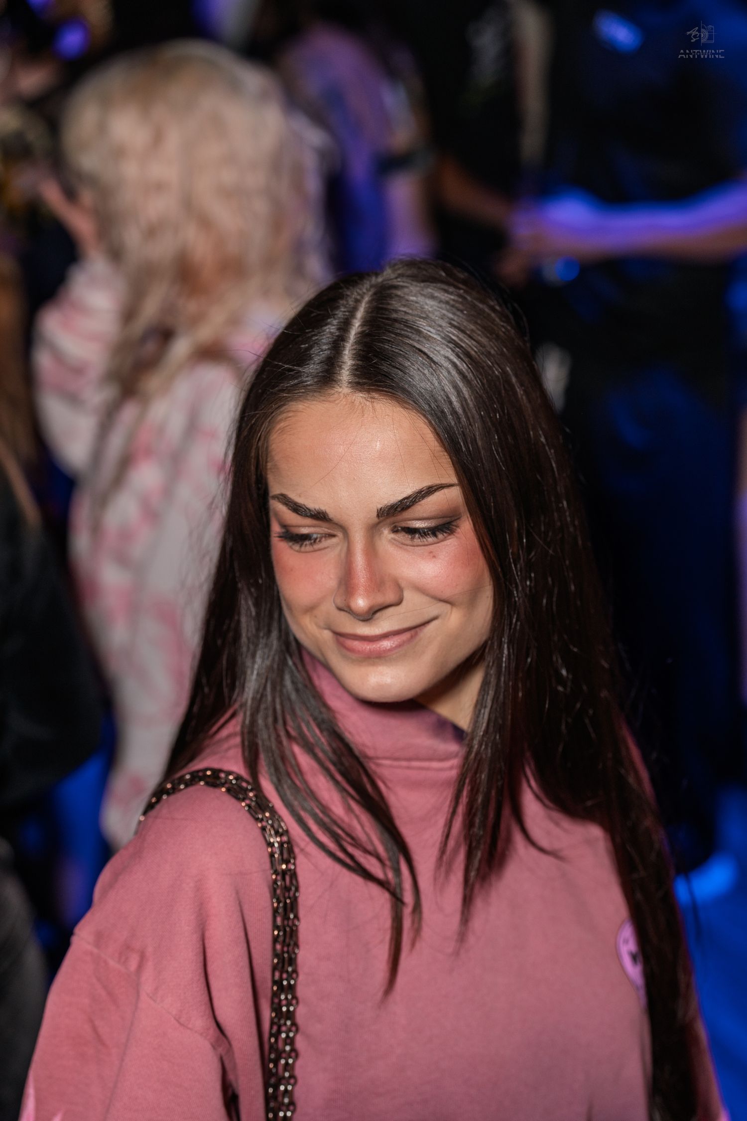 Brunette woman in pink hoodie looking down at a crowded nightclub.