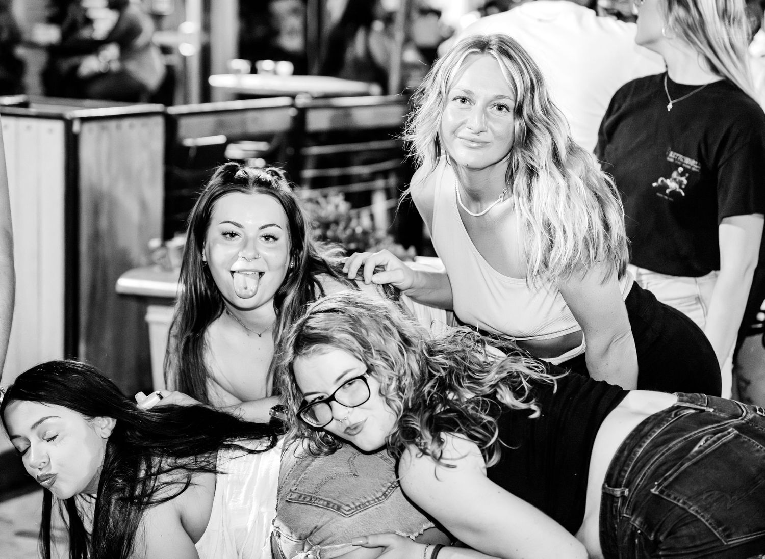 A fun black and white photo of four women laughing and posing at a party.