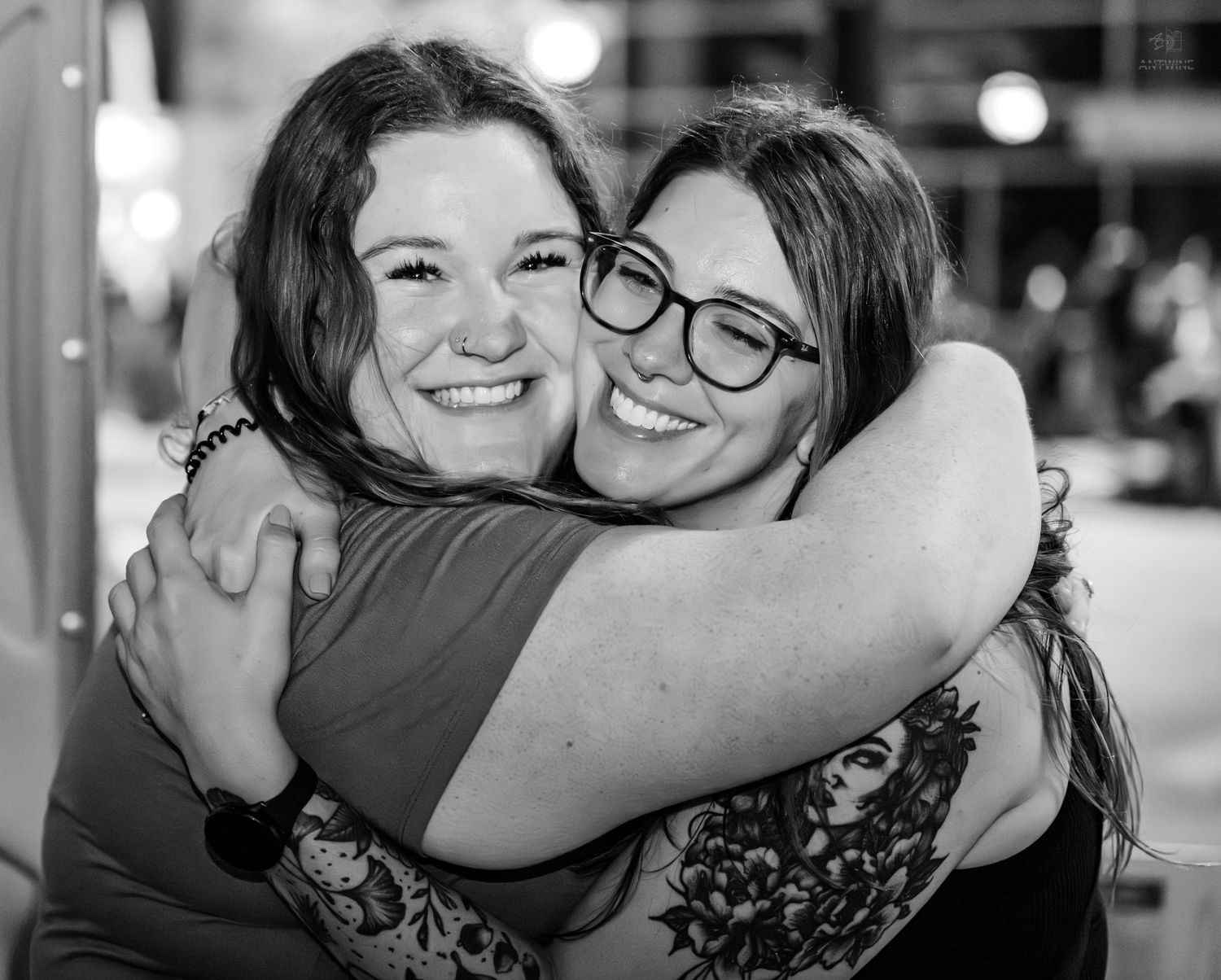 Two women smiling and hugging warmly in a black and white photo at a social event.