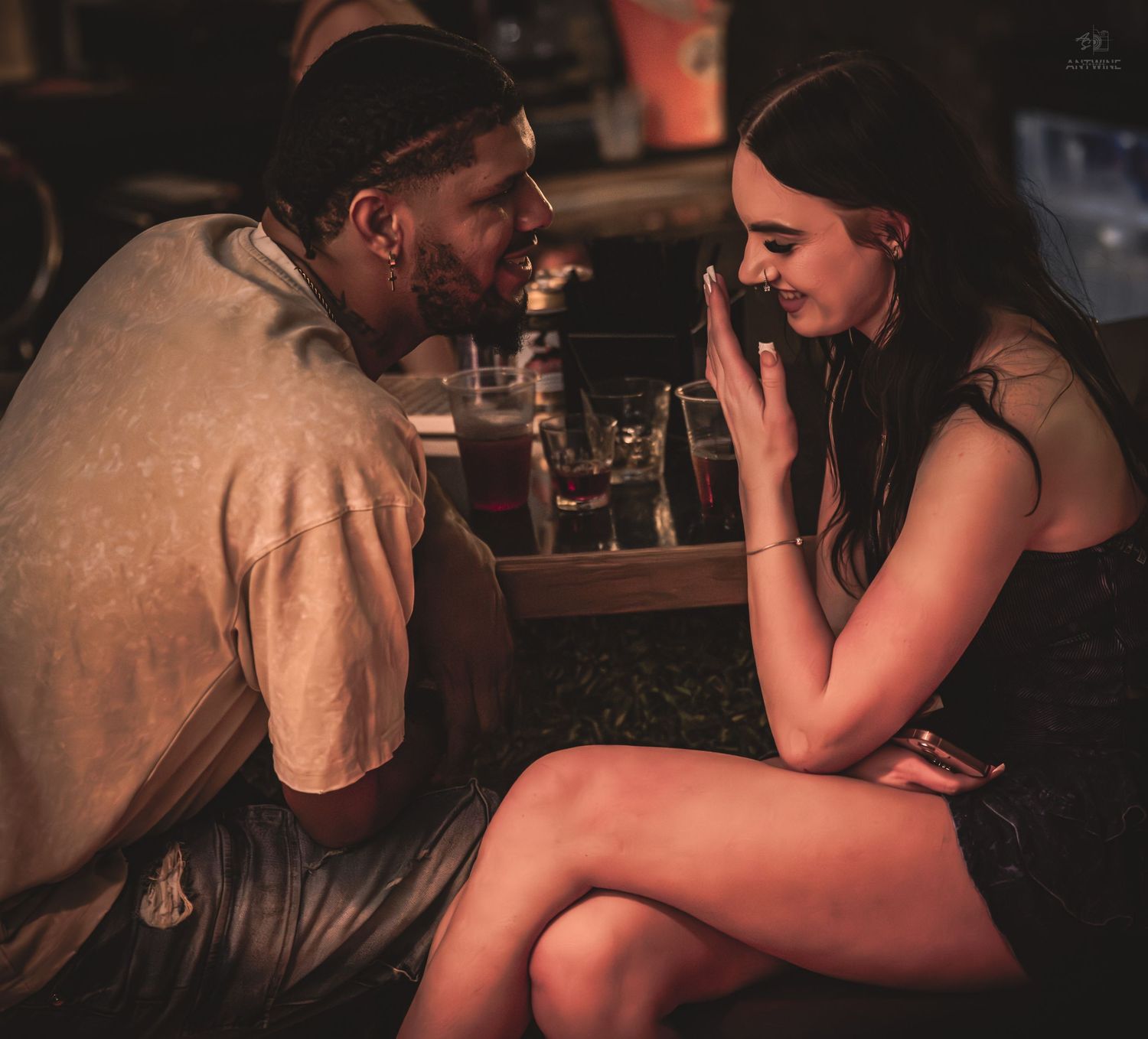 A man and woman engage in an intimate conversation at a cozy, warmly lit bar setting.