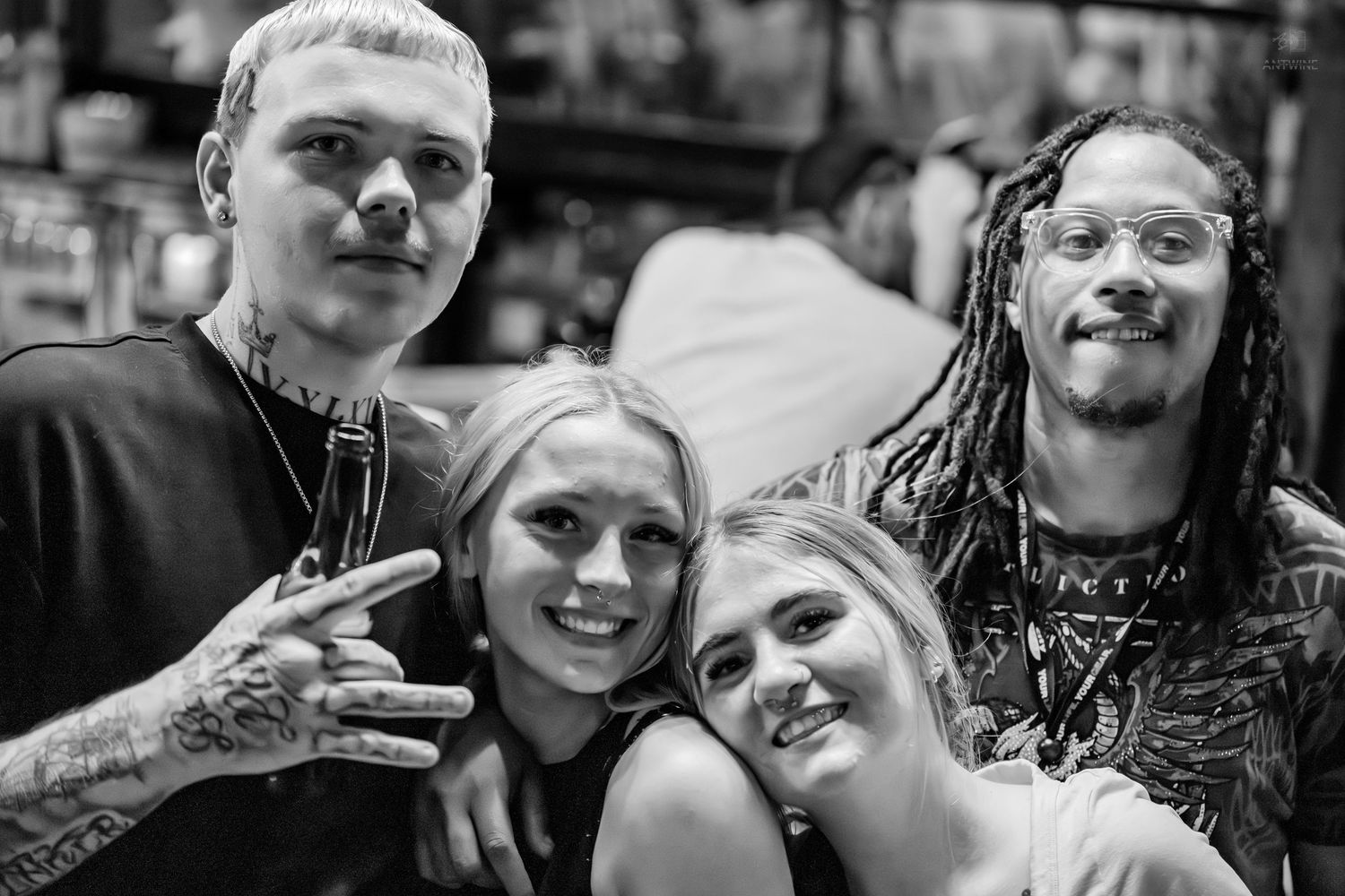 Group of four friends posing together smiling at a bar in black and white photo.