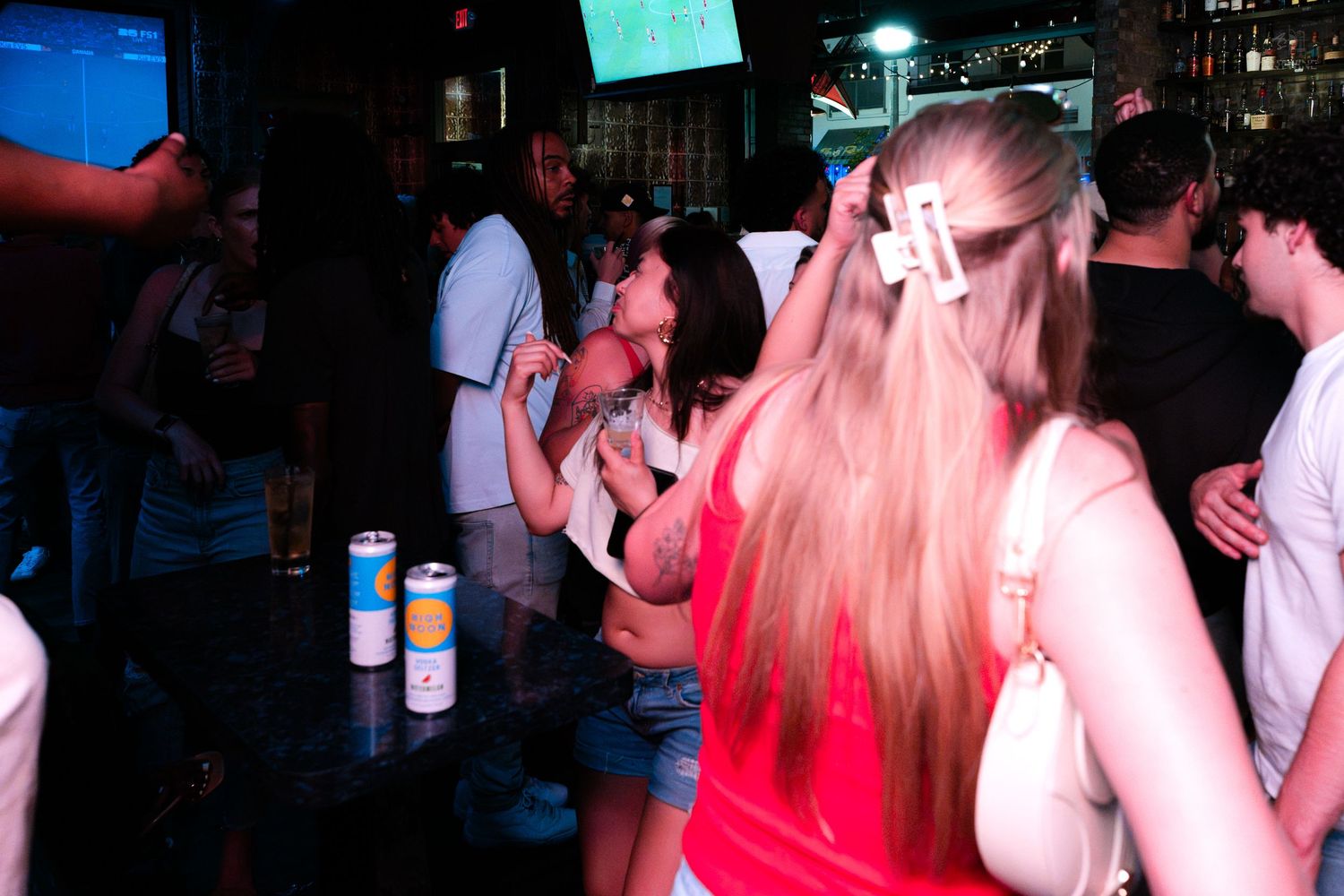 People dancing and socializing inside a dimly lit bar with drinks on the counter.