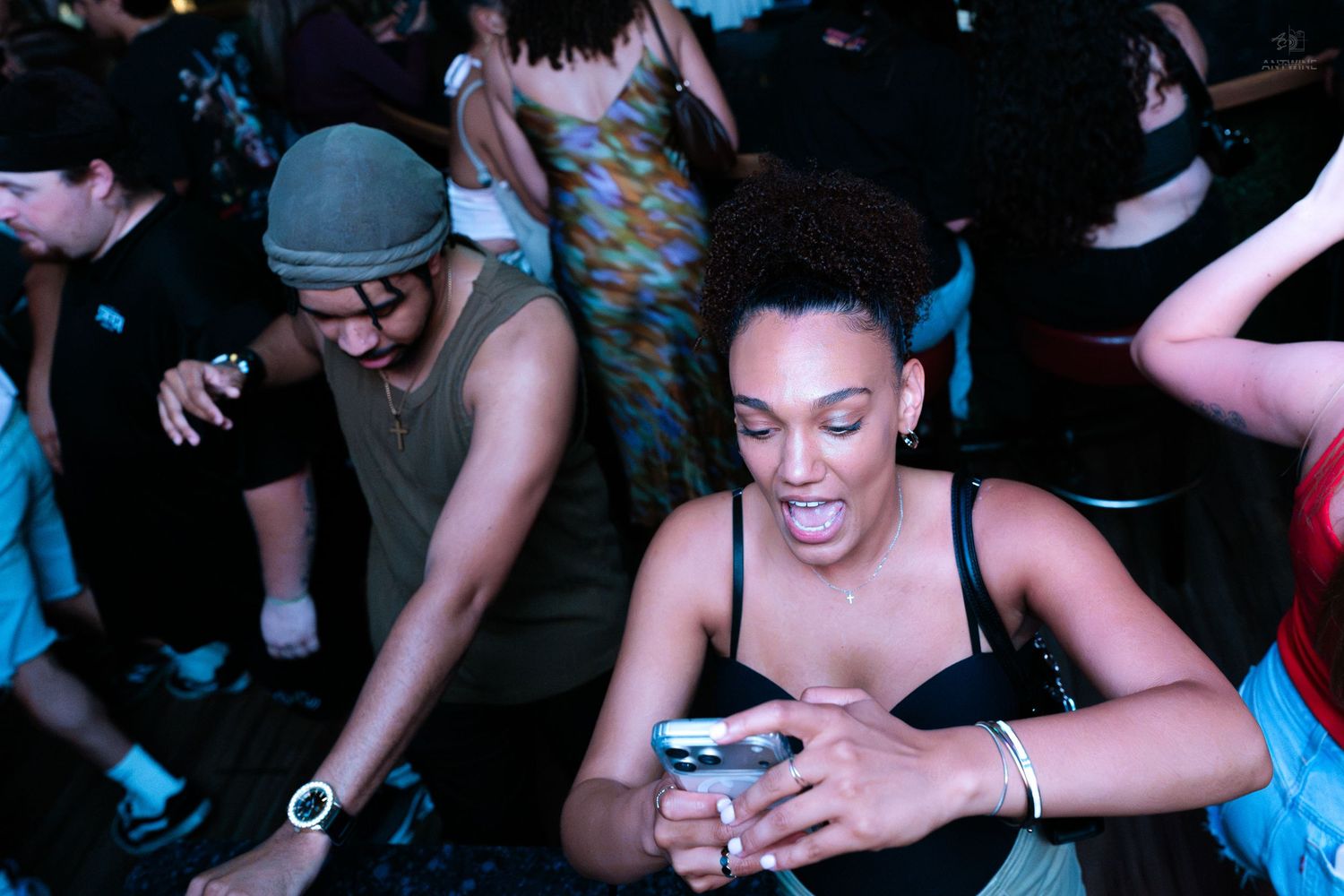 Woman smiling at her phone while dancing at a vibrant nightclub party.