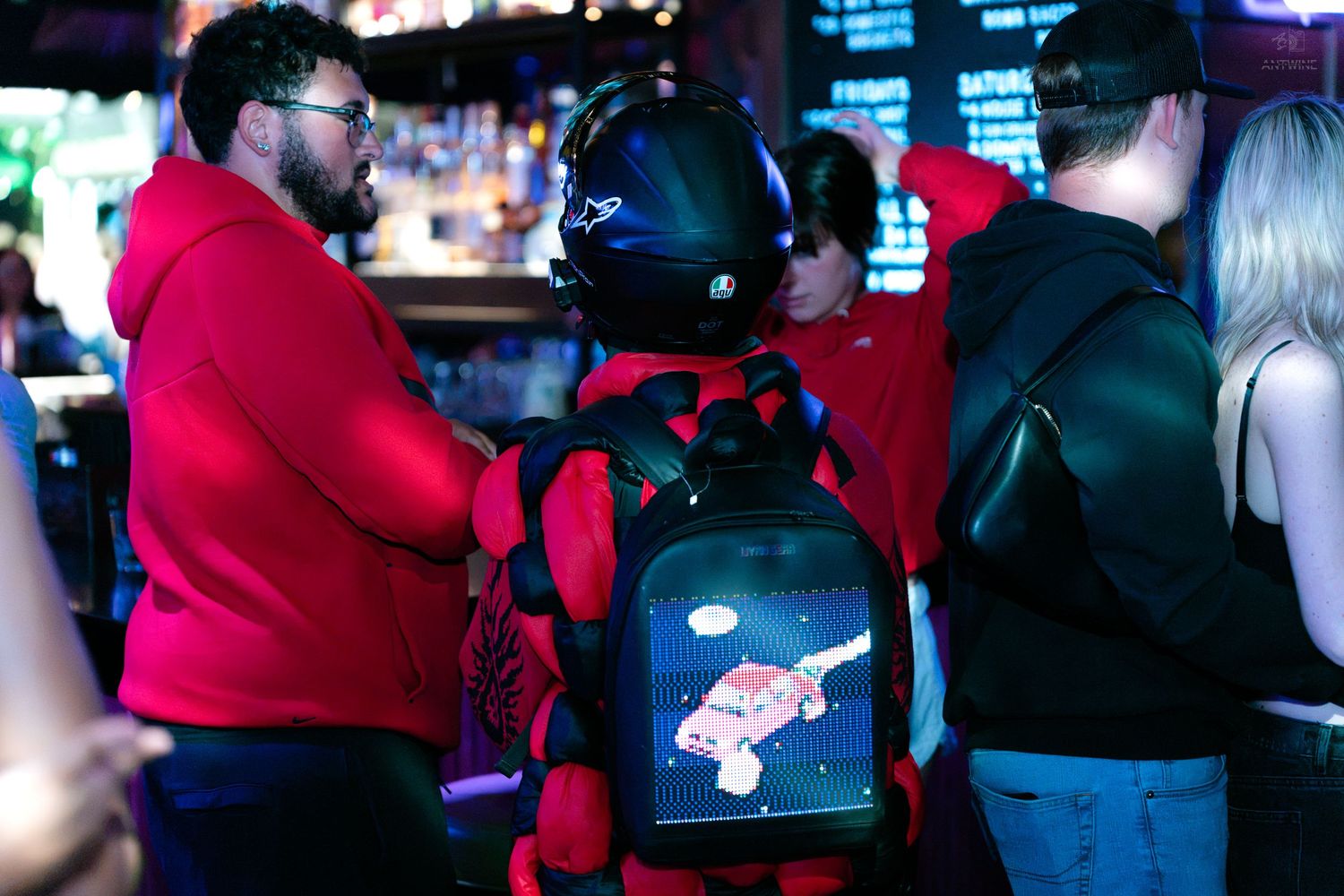 Person in red astronaut costume with LED display backpack standing at a bar.