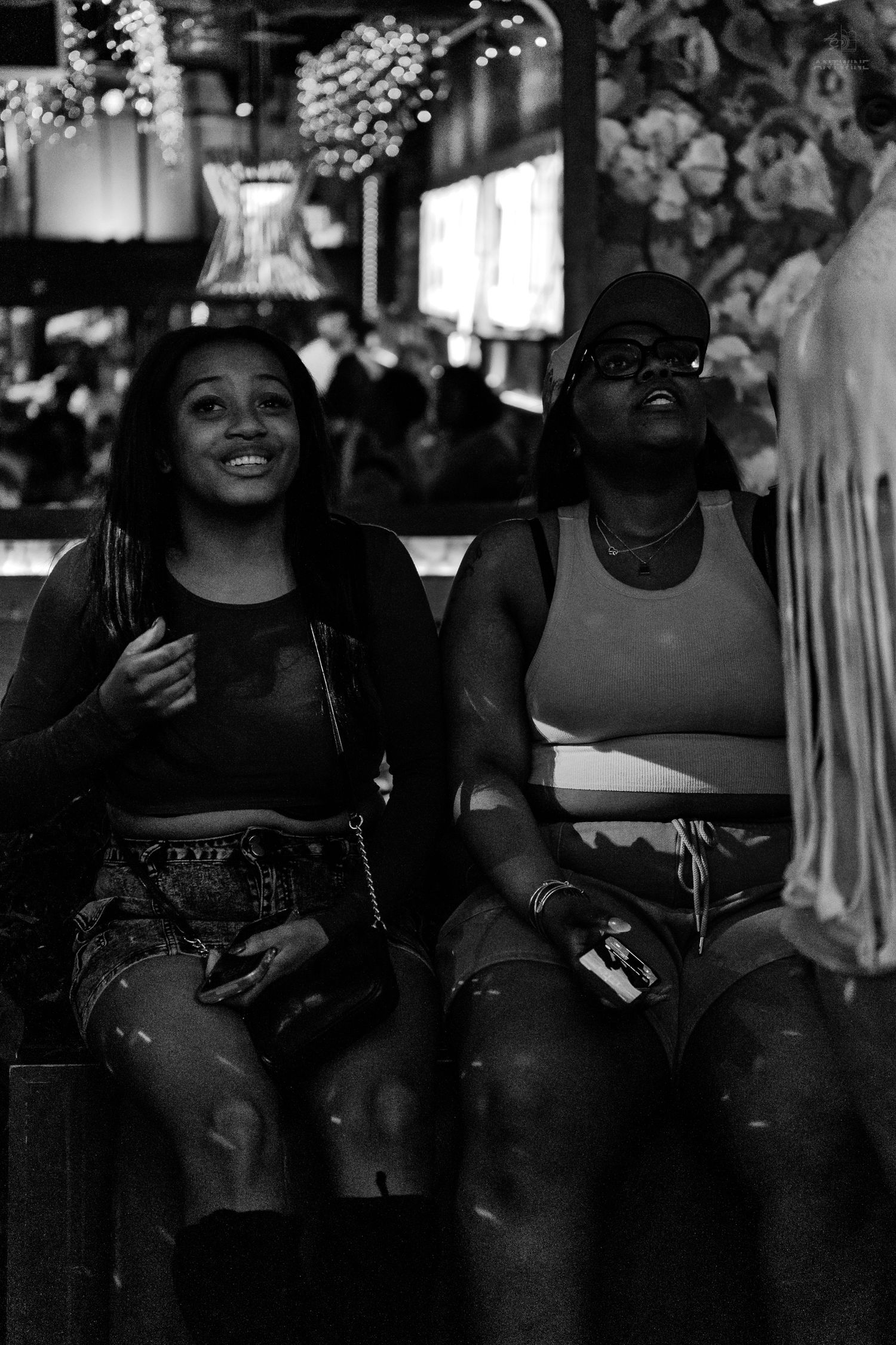 Two women sitting and laughing together at a lively nightclub event.
