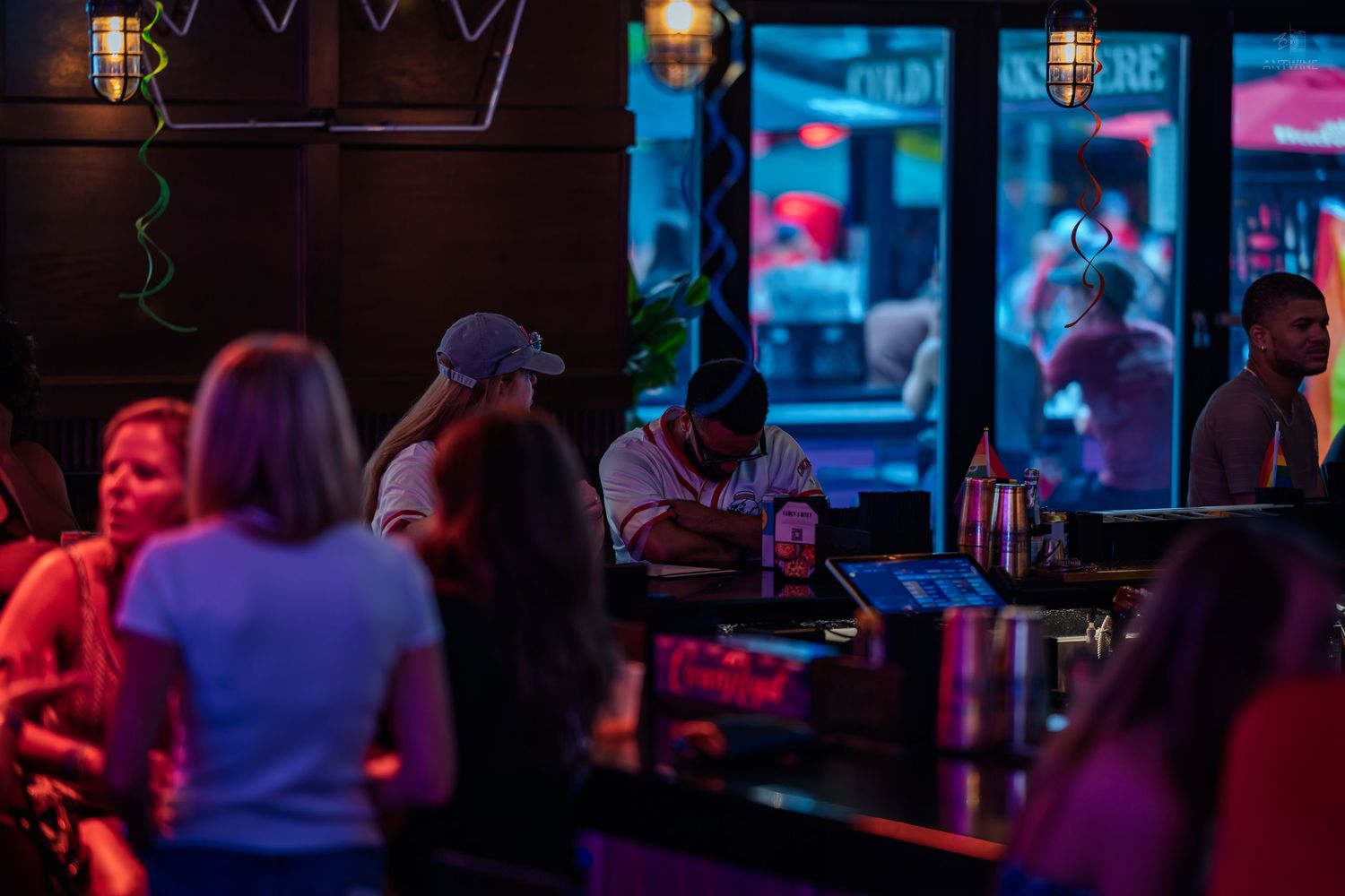 Group of people socializing inside a dimly lit bar with neon purple lighting.