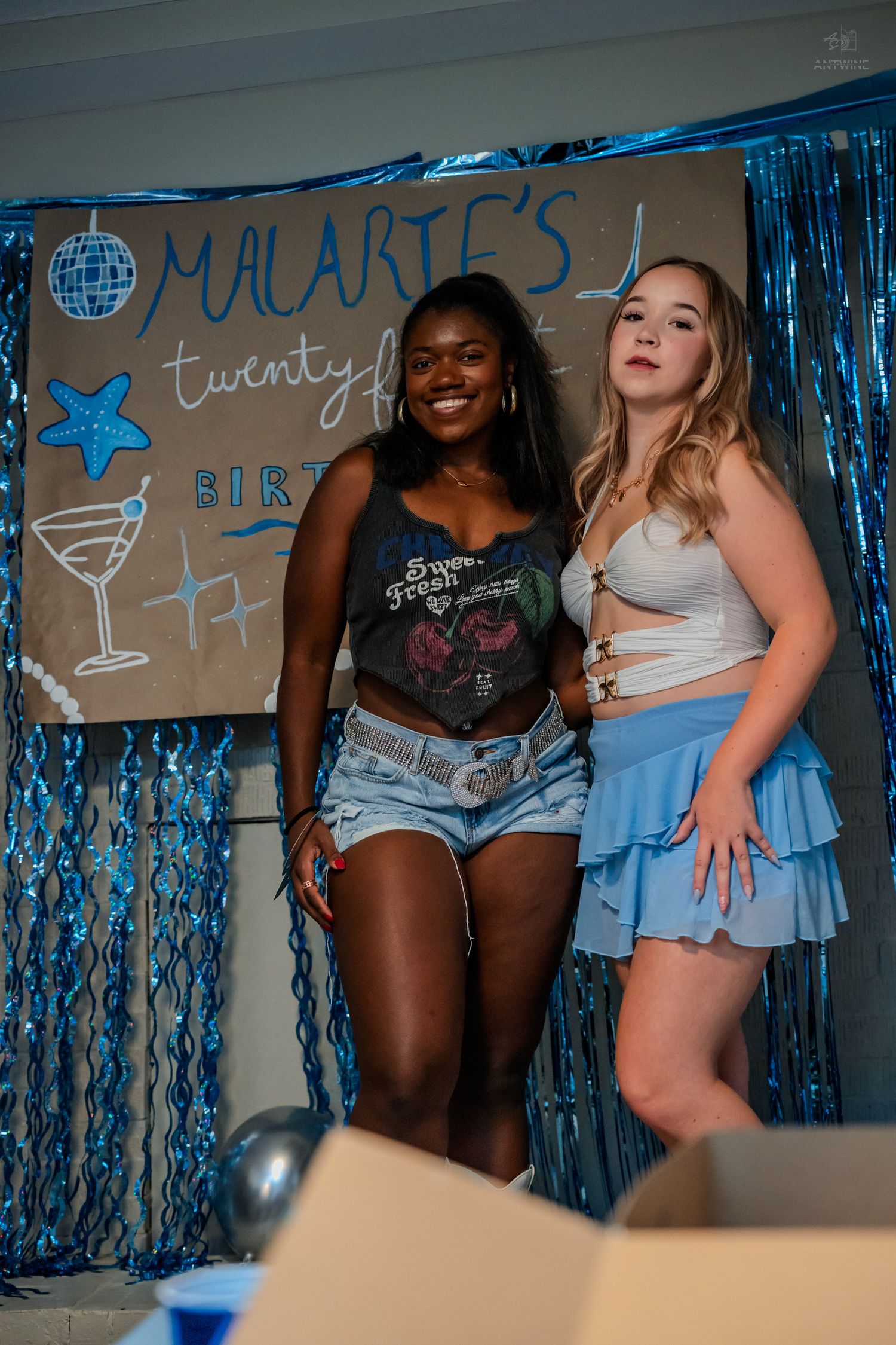 Two women smiling together at Malarie's 21st birthday party with blue foil curtain backdrop.