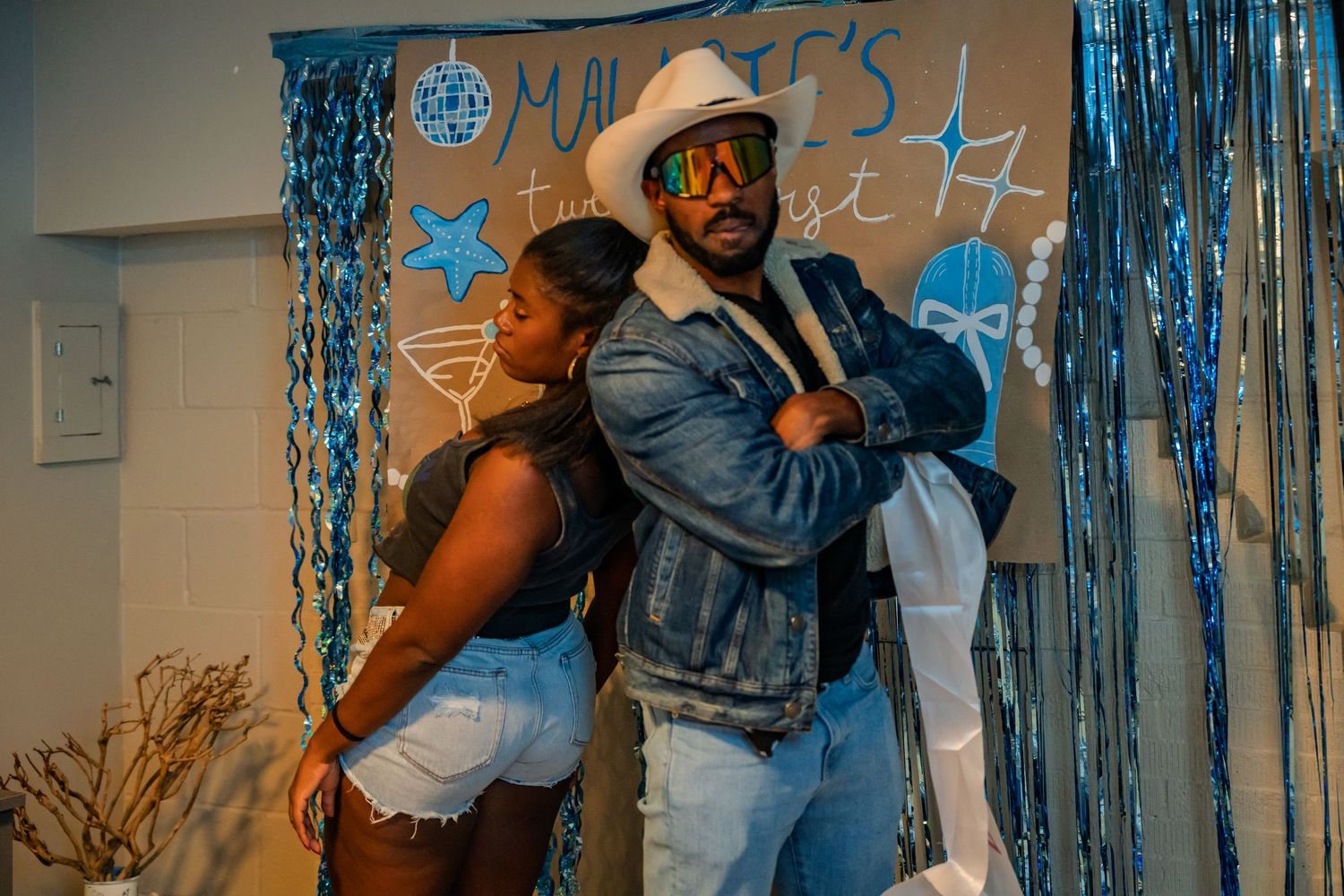 Couple posing back-to-back confidently at a blue tinsel-decorated 21st birthday party.
