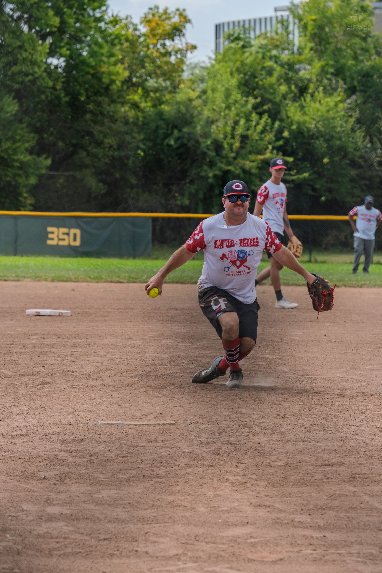 A fielder in a Battle of the Badges jersey throws a yellow softball during a game.