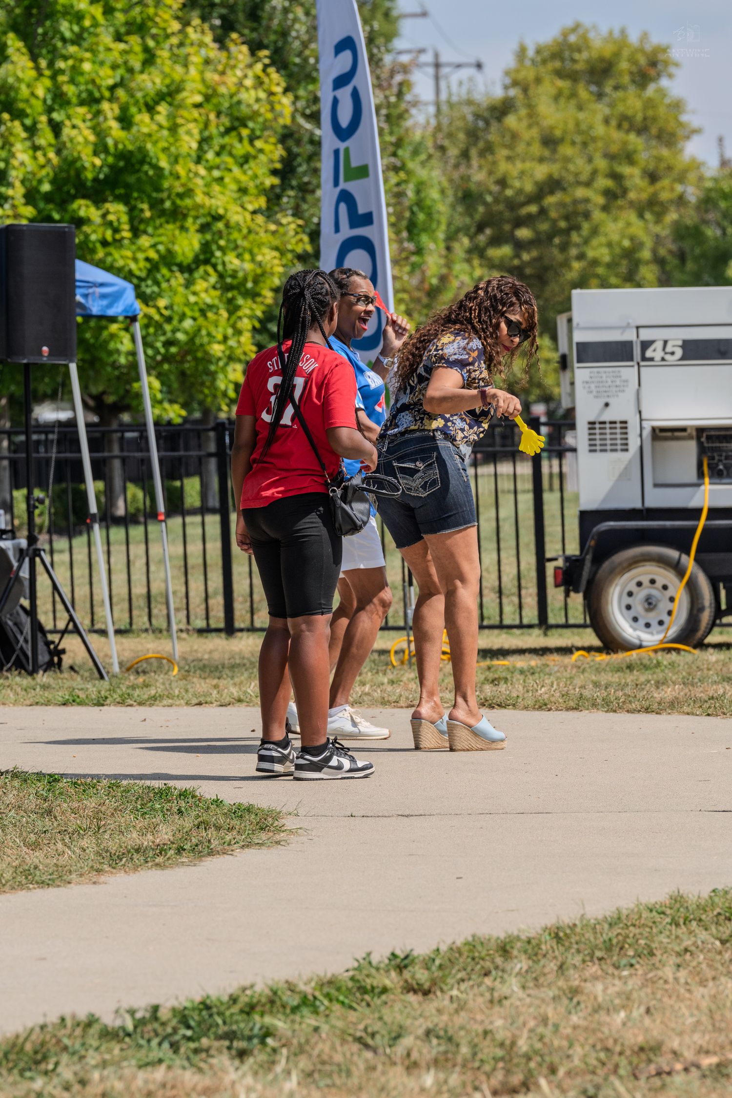 Three women standing together near a COPEC banner at an outdoor charity softball game event.