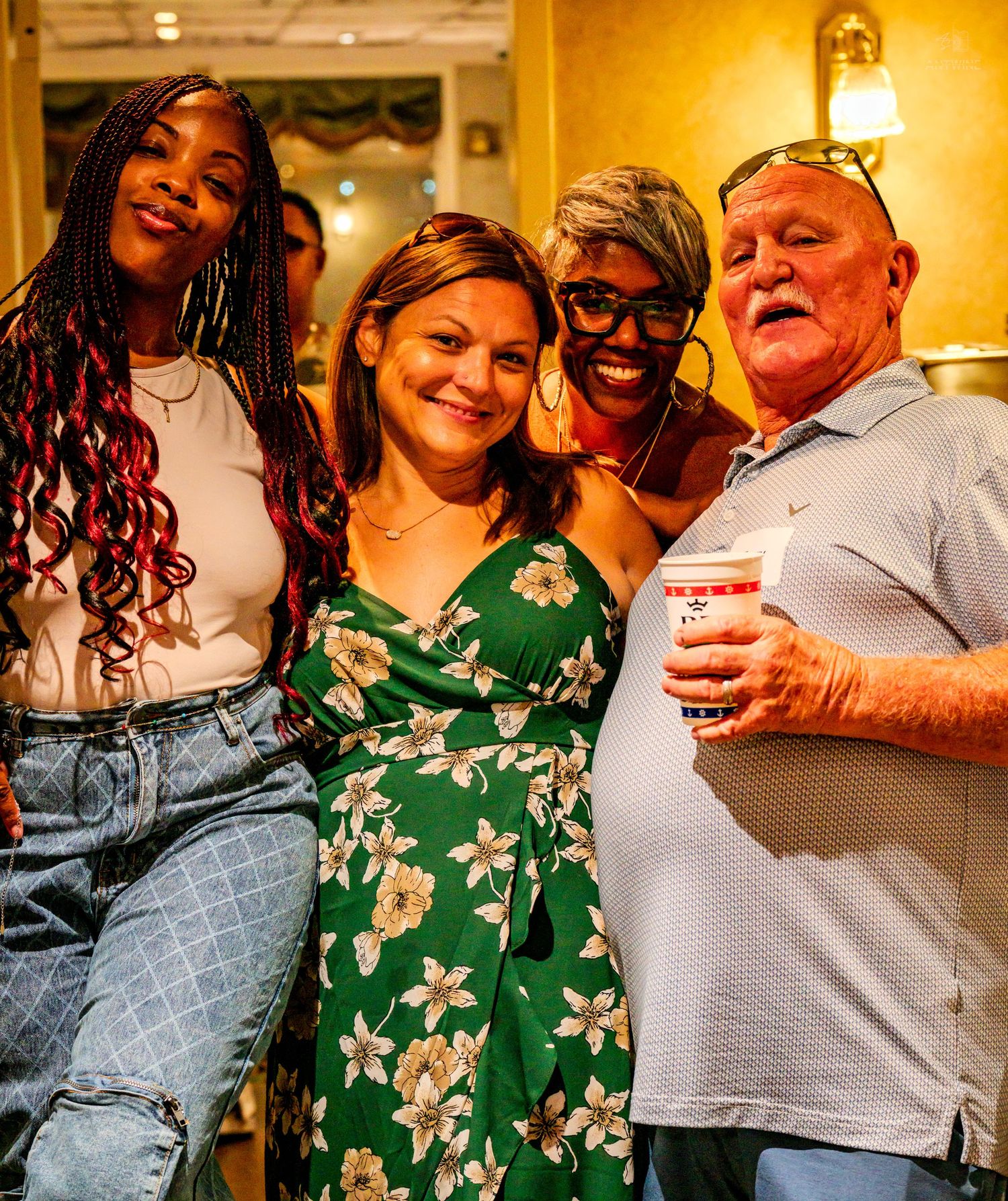 Four smiling people pose together at a festive indoor social gathering event.