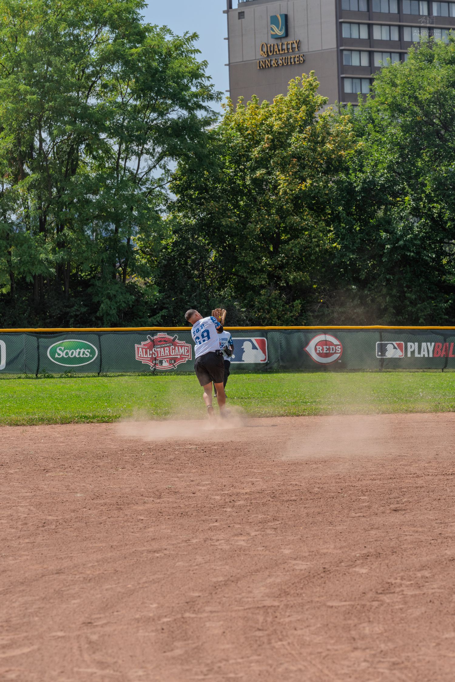 Softball player sliding into base creating a dust cloud near the outfield wall during a game.