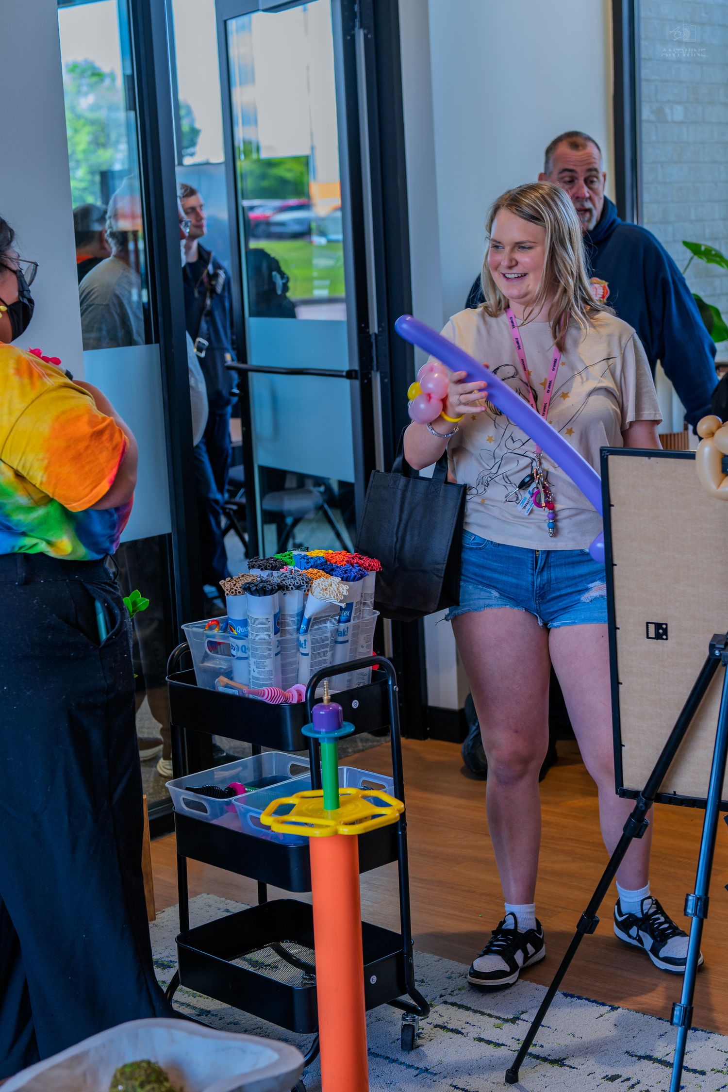 Smiling woman holds a purple balloon animal at a fun indoor balloon art activity event.