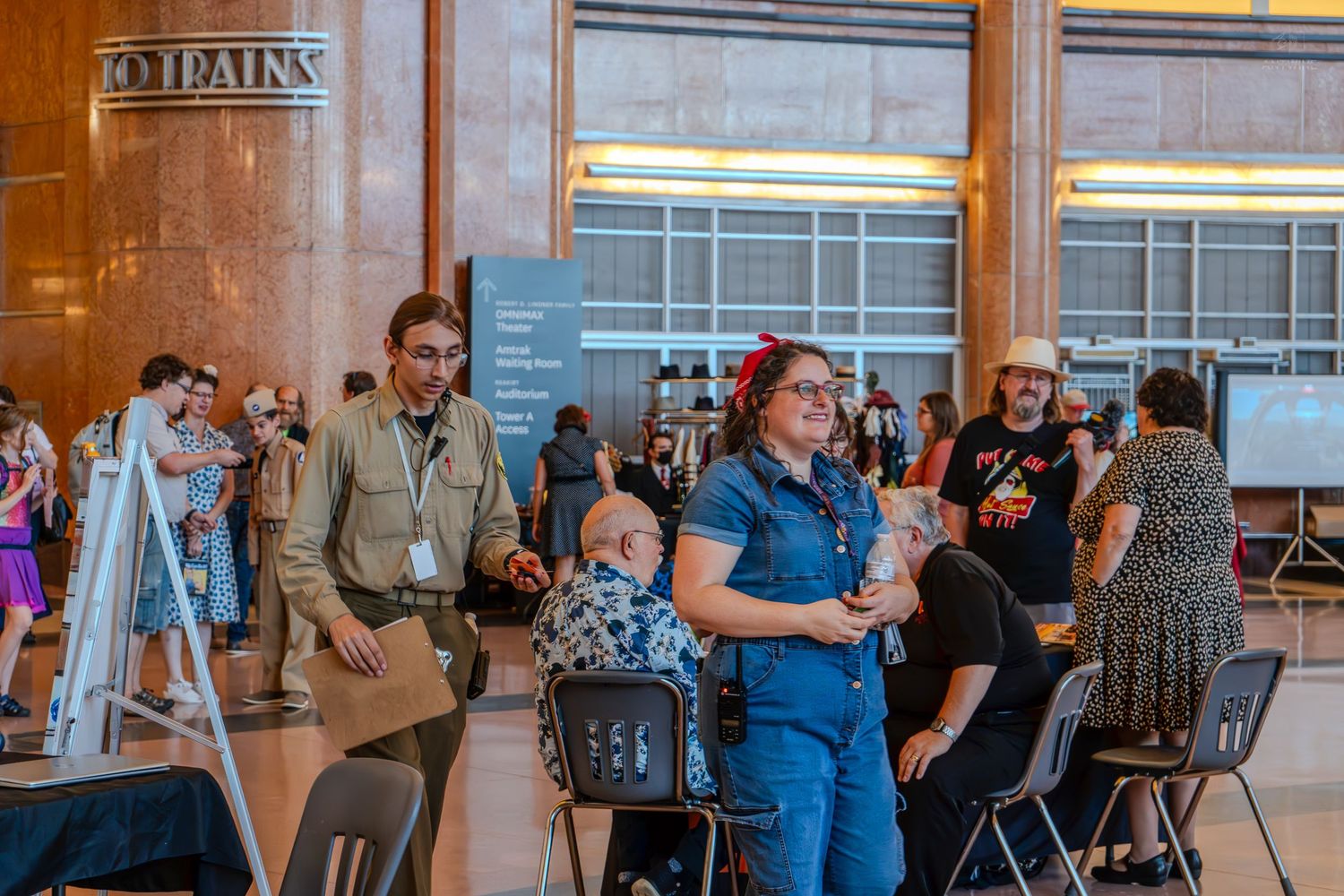 People mingling at an indoor event in a grand hall with marble columns and exhibit displays.