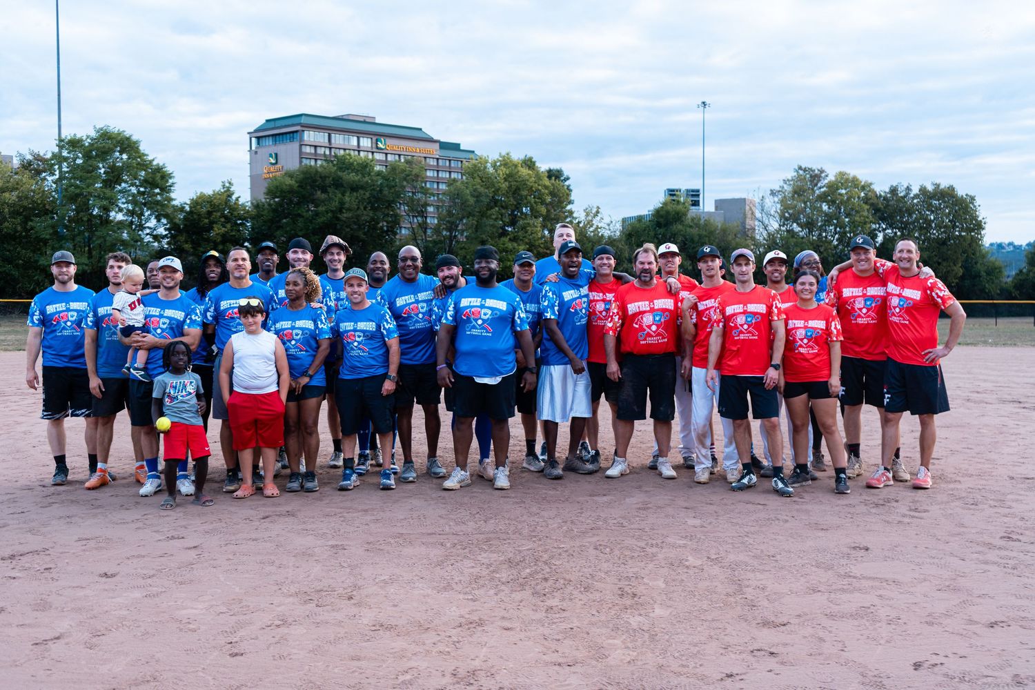 Two softball teams pose together on a field wearing blue and red jerseys.