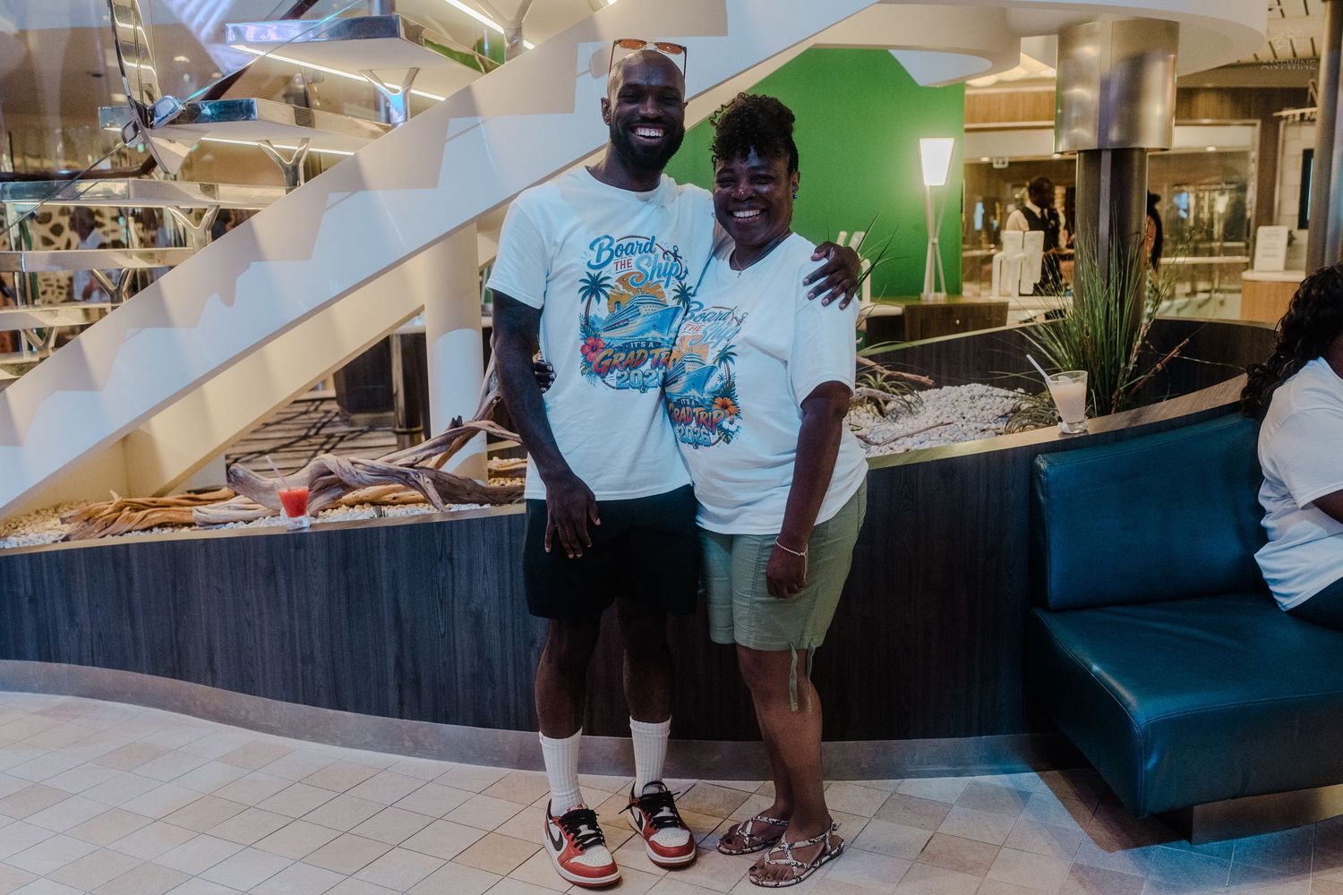 A tall man and a woman in matching light blue graphic tees pose together on a cruise ship.