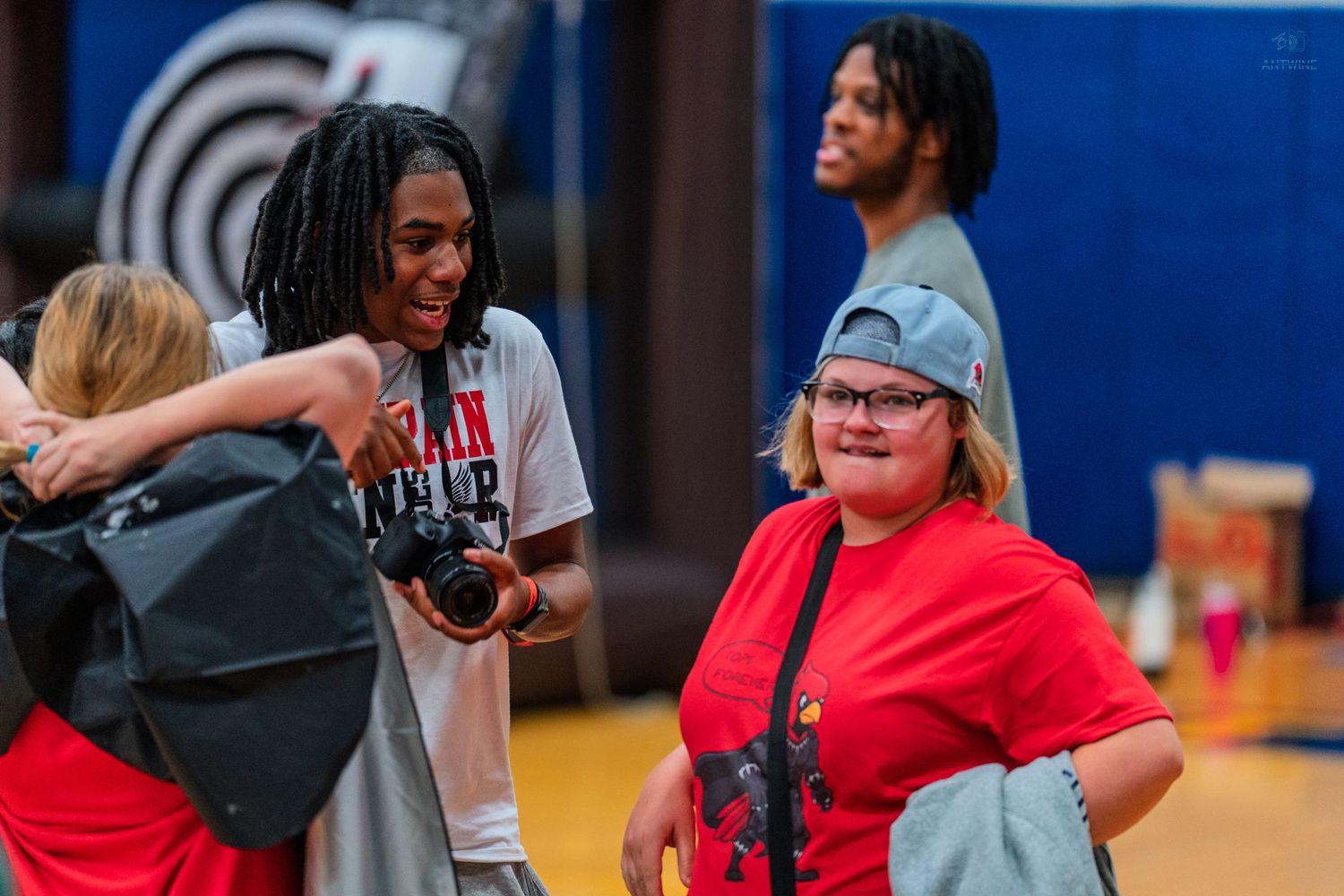 Two smiling young people in red shirts share a joyful moment in a gymnasium during a sports event.