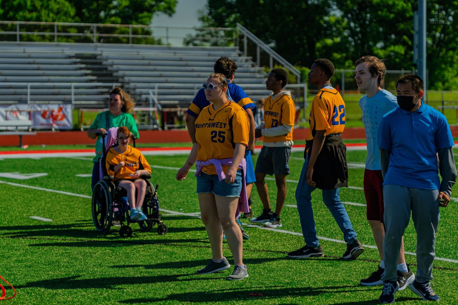 Students in yellow jerseys participate in a flag football event on a green turf field, including a wheelchair user.
