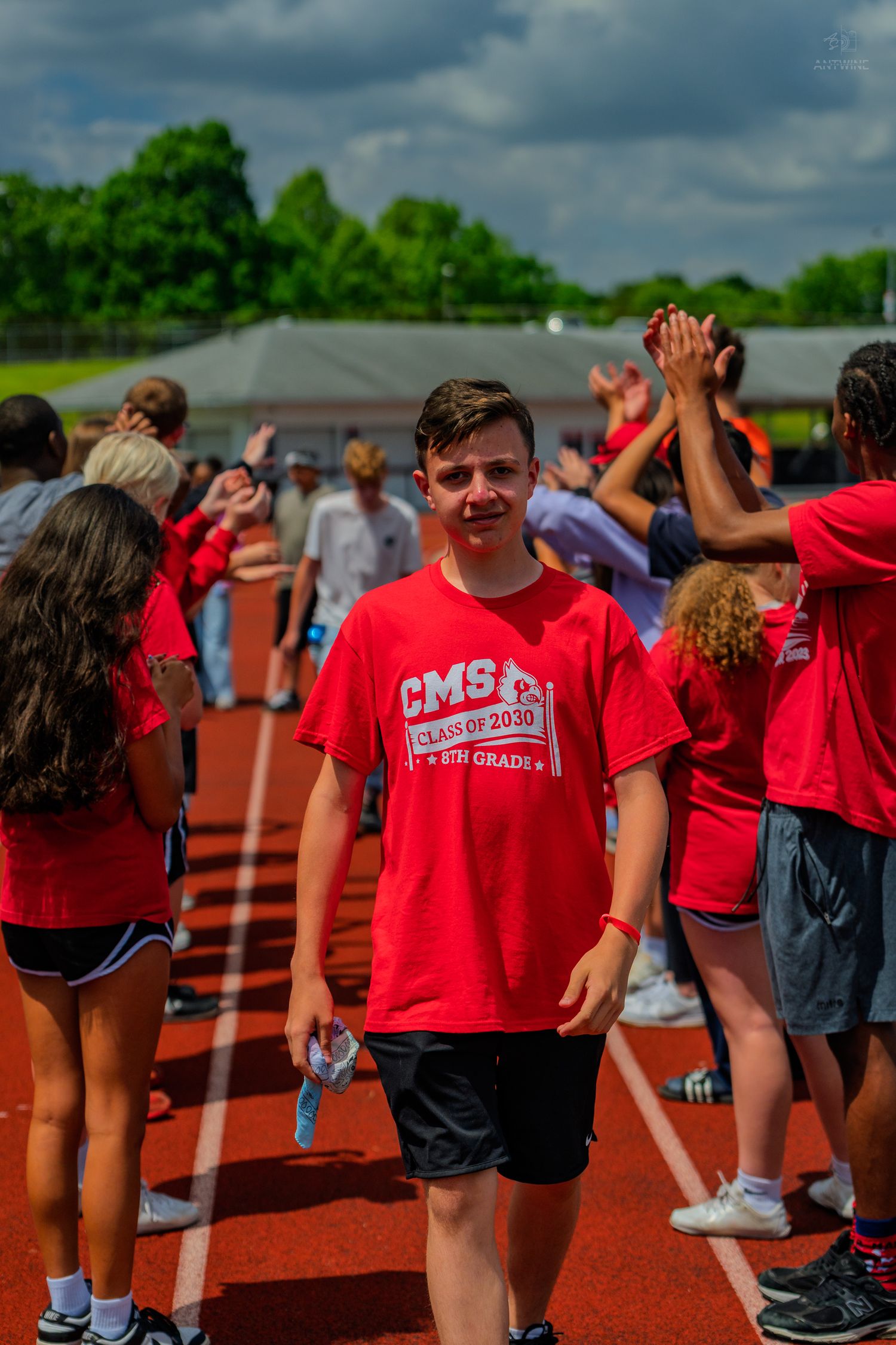Student in red CMS Class of 2030 shirt walks through high-five line on school track during outdoor event.