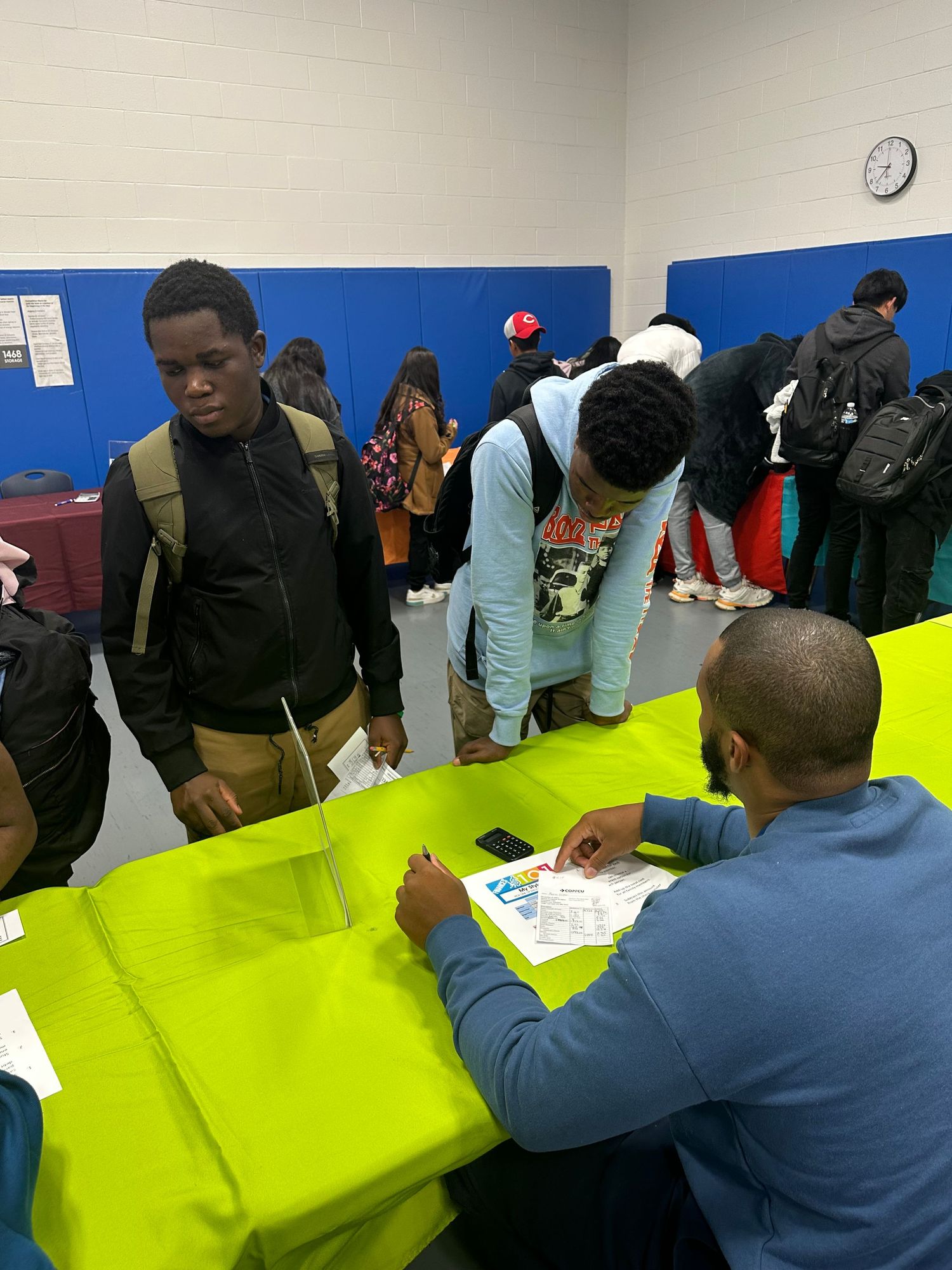 Students gather at bright green tables during a school career fair event in a gymnasium.