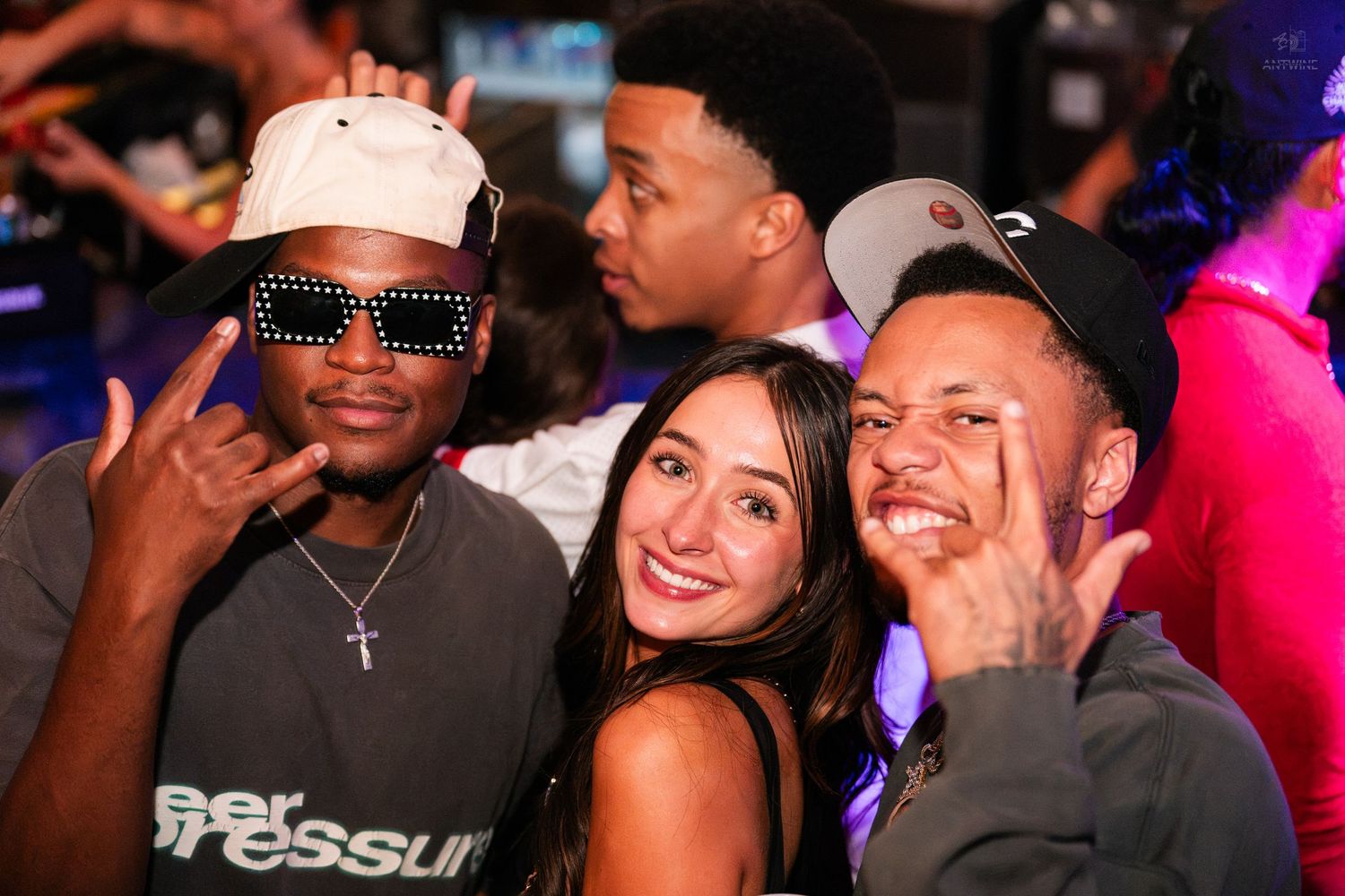 Three friends smiling and posing together under colorful nightclub lights.