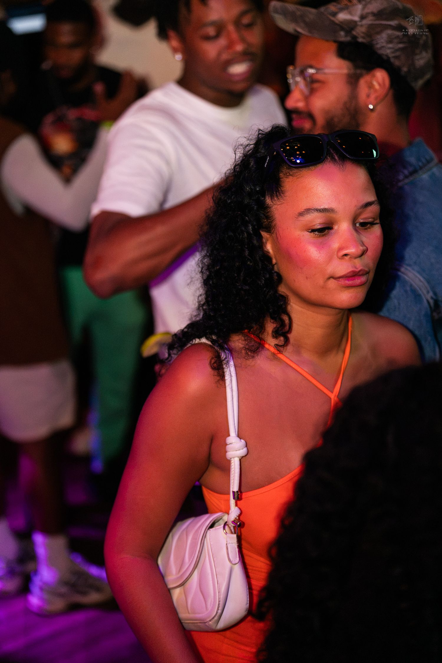 Young woman in an orange dress with a white bag at a crowded party.