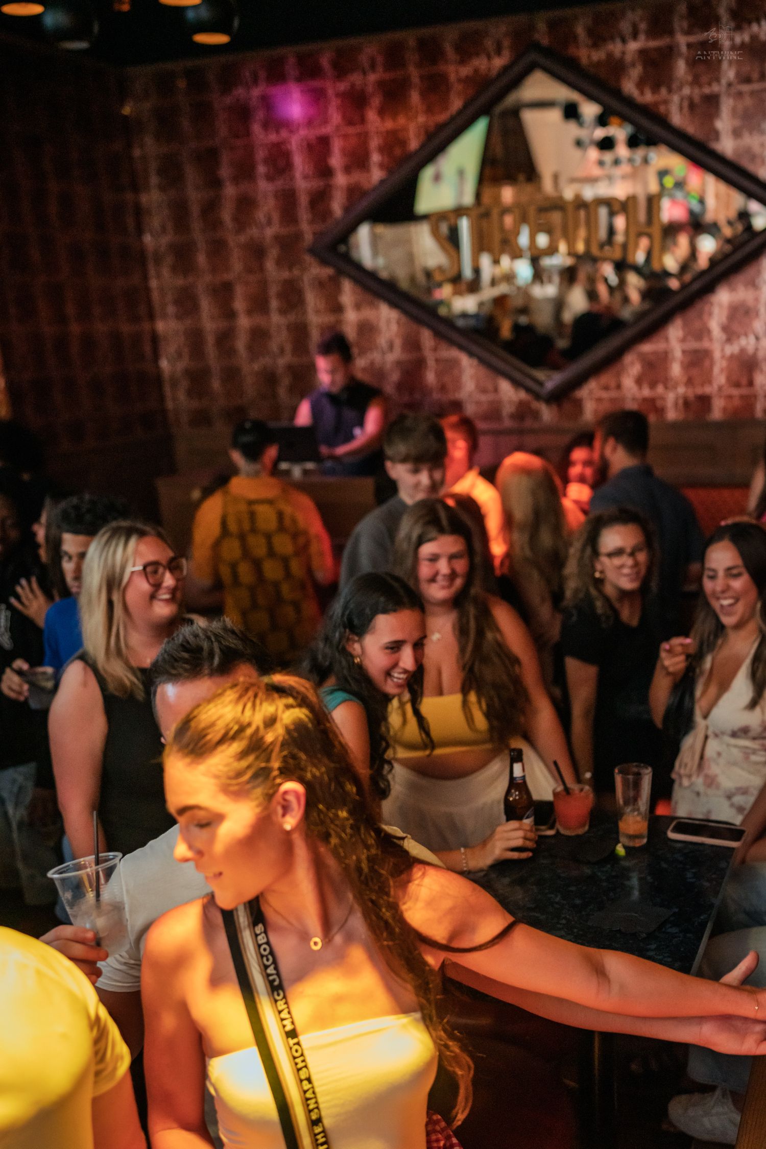 Women smiling and socializing at a warmly lit bar with a decorative diamond mirror.
