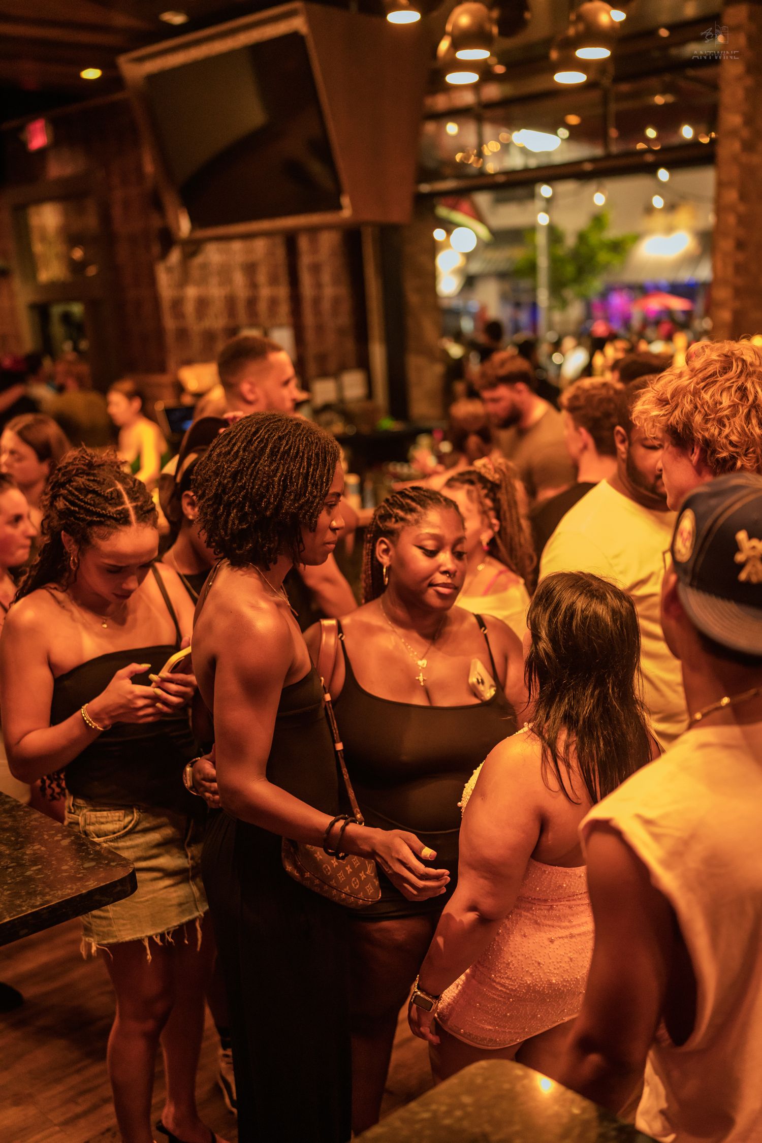 Group of young women in black outfits socialize and mingle in a warmly lit crowded nightclub venue.