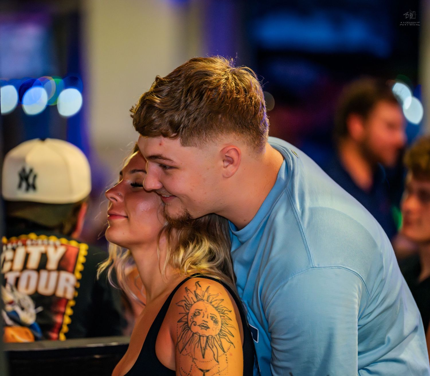 A couple shares a tender moment at a lively bar or nightclub event.
