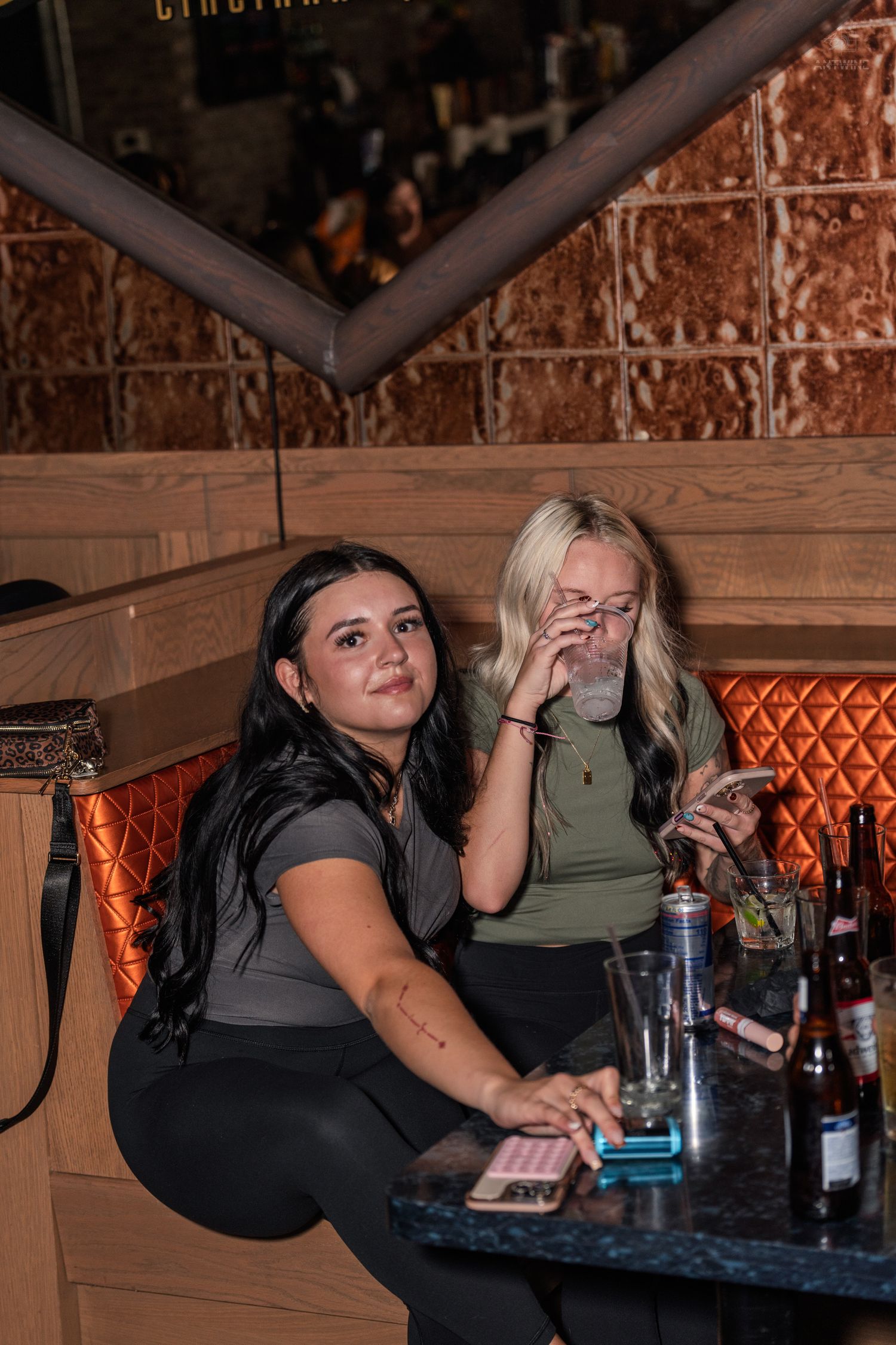 Two women sitting in an orange quilted booth at a Cincinnati nightclub with drinks.
