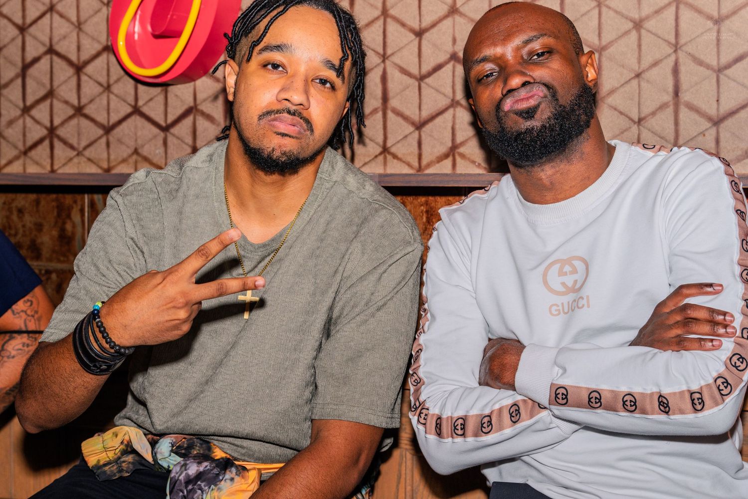 Two men posing together at a nightclub, one making a peace sign.