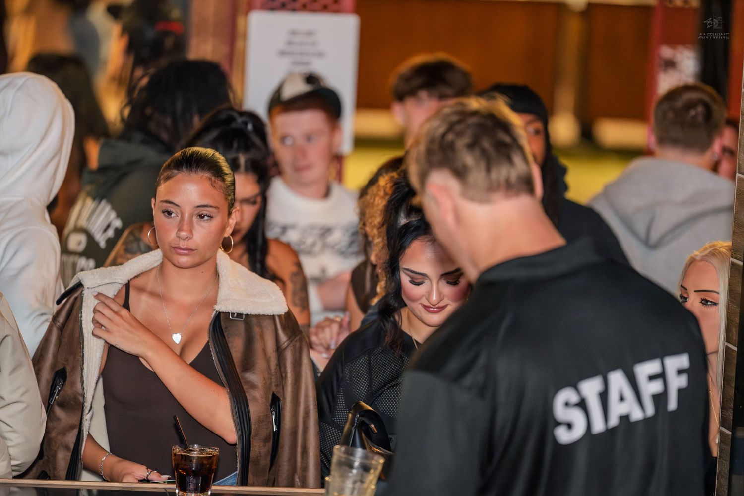 Group of young people socializing outdoors near a staff member at a night event.