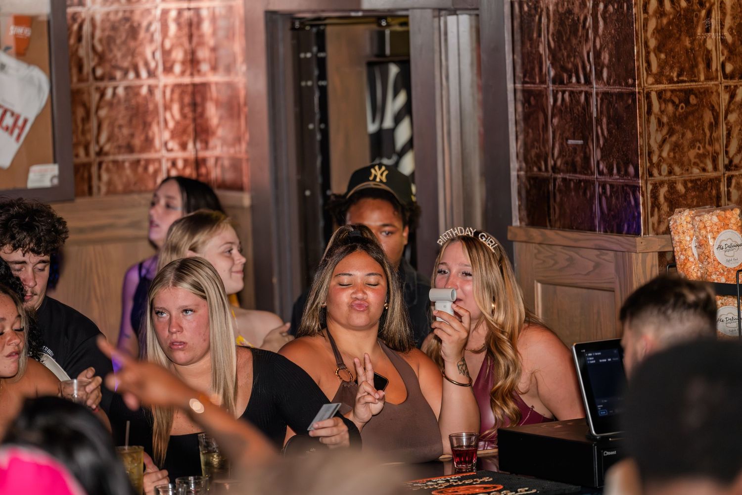 Group of young women socializing at a bar with copper walls and warm lighting.