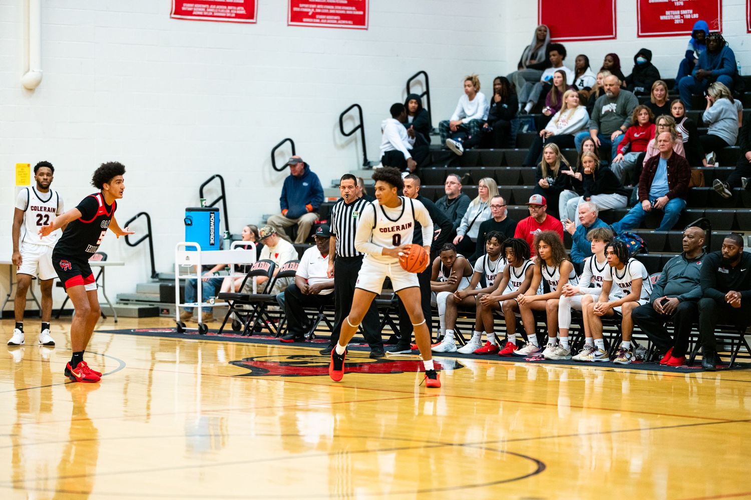 A basketball player in white dribbles near the three-point line during a high school game with fans watching.