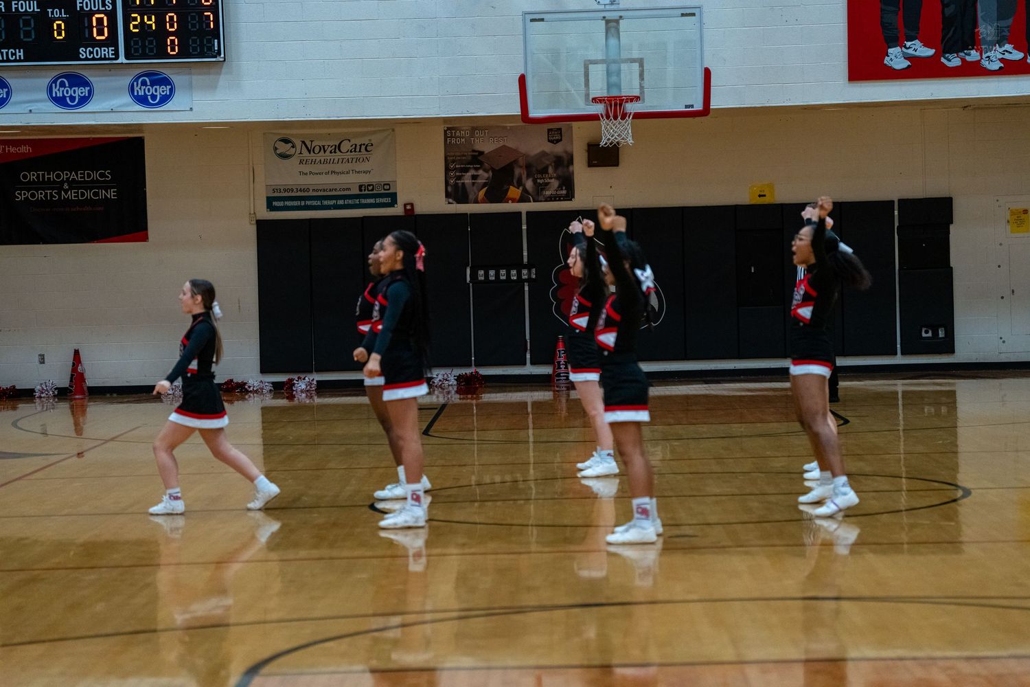 Four cheerleaders in black and red uniforms perform a dance routine on a basketball court.