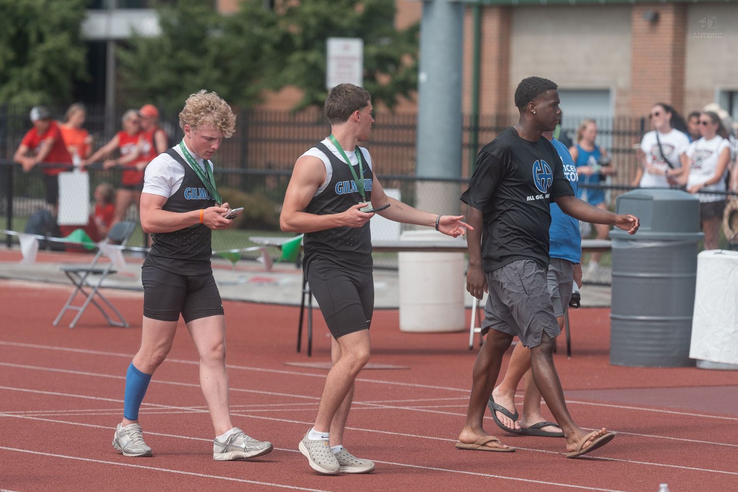 Three male athletes in green and black uniforms walk on a red track after a relay race event.