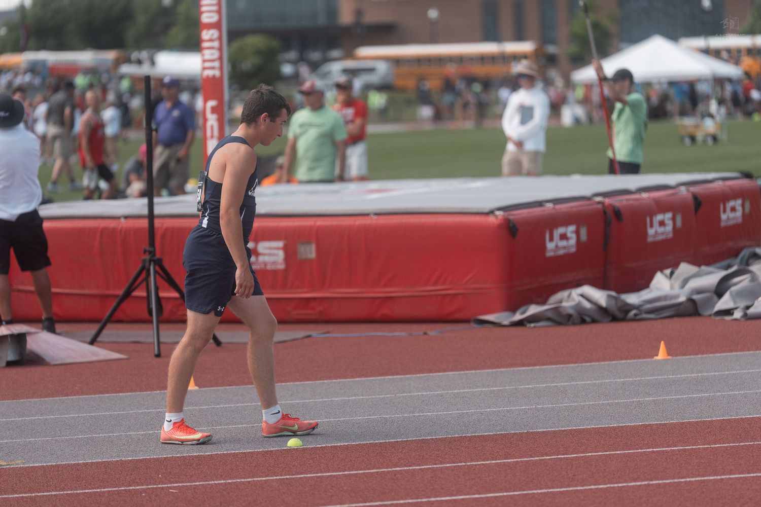 Young female athlete in navy uniform stands on a red track at an outdoor track and field competition.