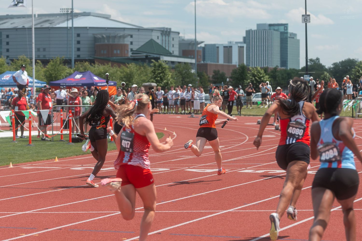 Multiple female athletes race on a red track at an OHSAA high school track and field championship event.