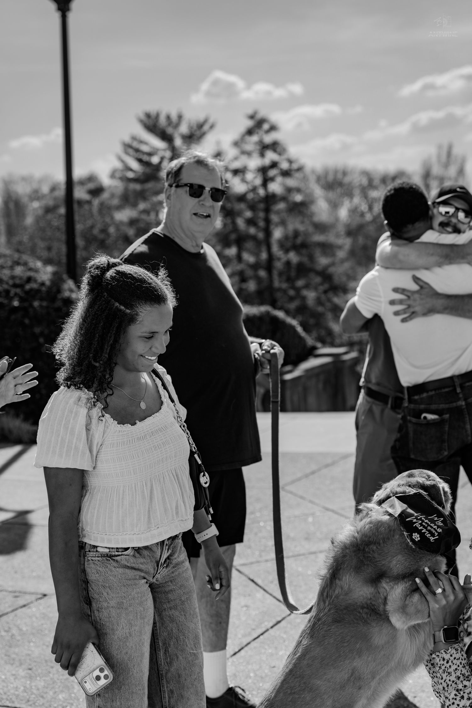 Black and white photo of a smiling girl in a white top standing near an older man and a dog.