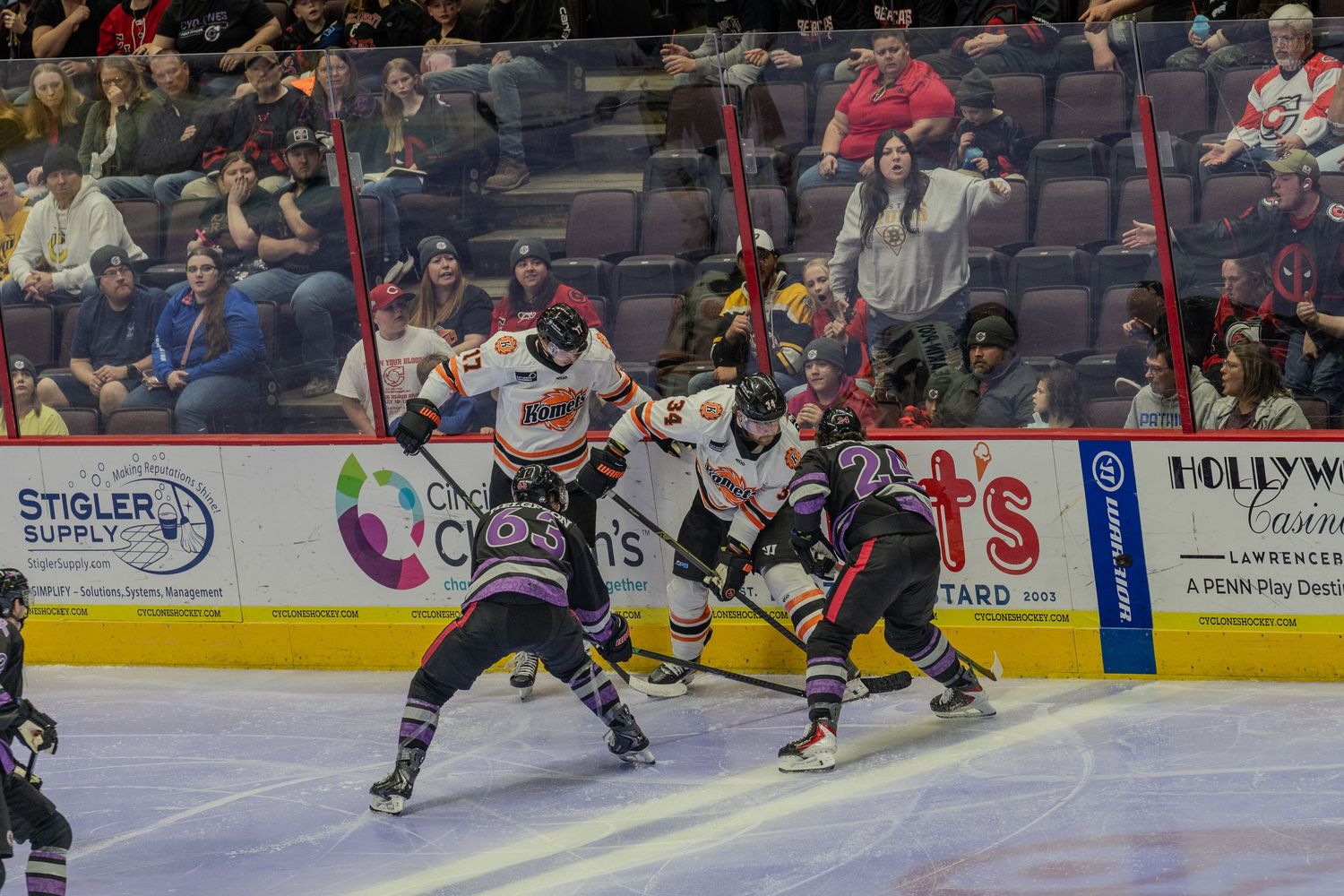 Hockey players fight for puck control during an intense ice hockey game in an indoor arena.