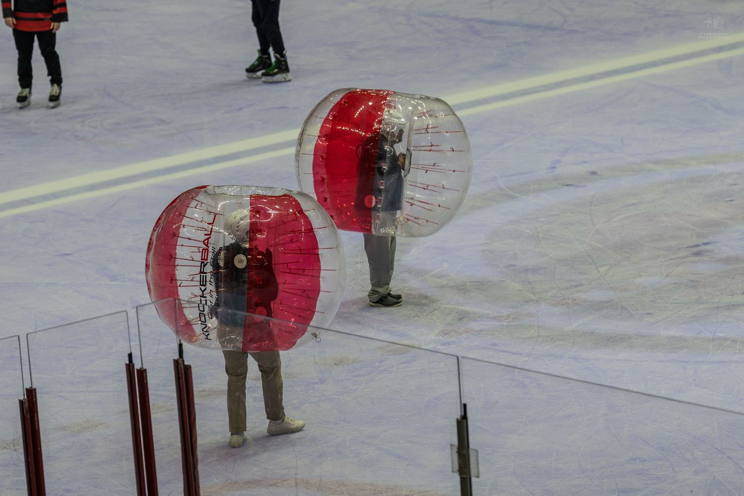 Two people inside large red inflatable bubble balls on an ice rink during an intermission activity.