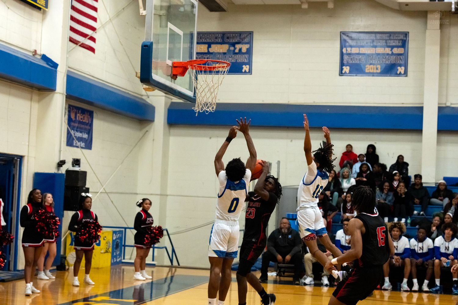 High school basketball player #0 shoots over defenders during an intense game in a blue gymnasium.