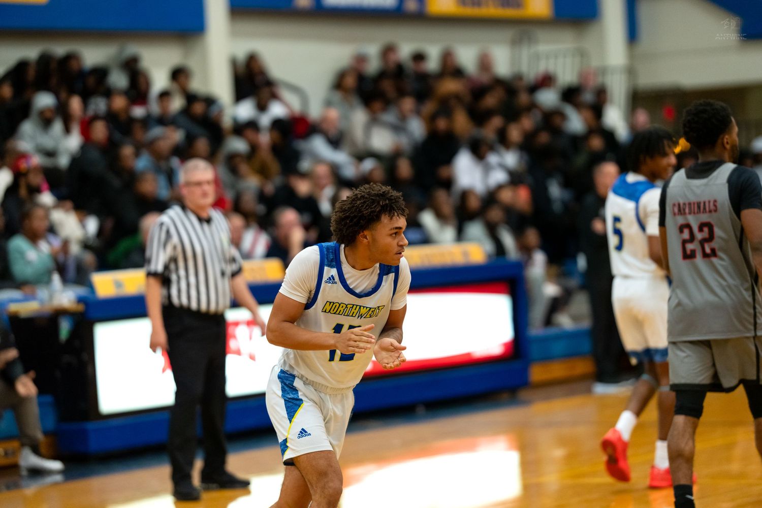 High school basketball player number 15 in blue uniform runs down court during competitive indoor game.