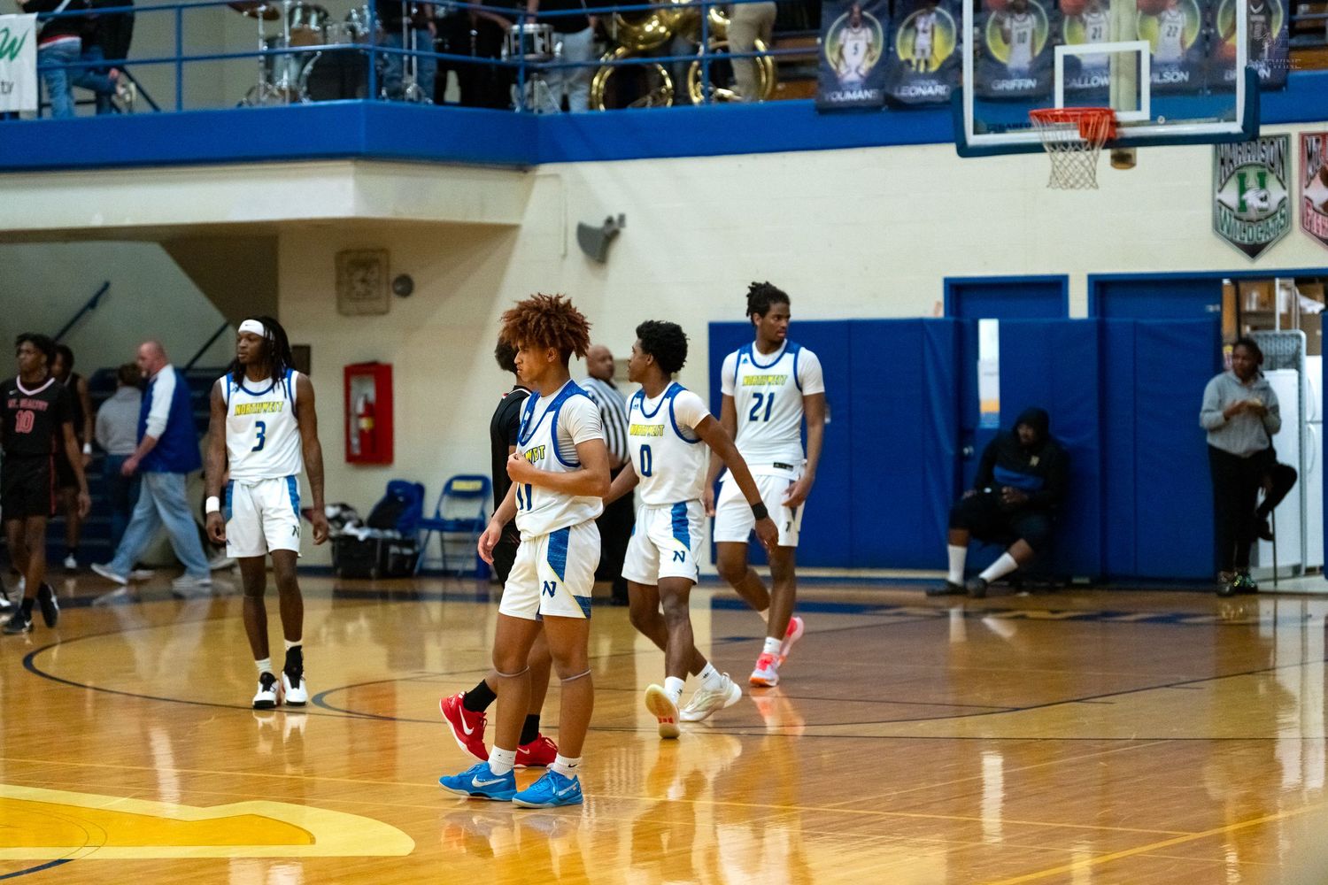 High school basketball players in blue and white uniforms gather on the court during a game in a school gymnasium.